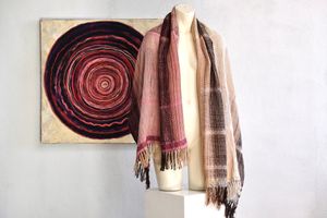Handwoven scarf naturally dyed shades of pink, brown and green on a white mannequin in a white gallery space