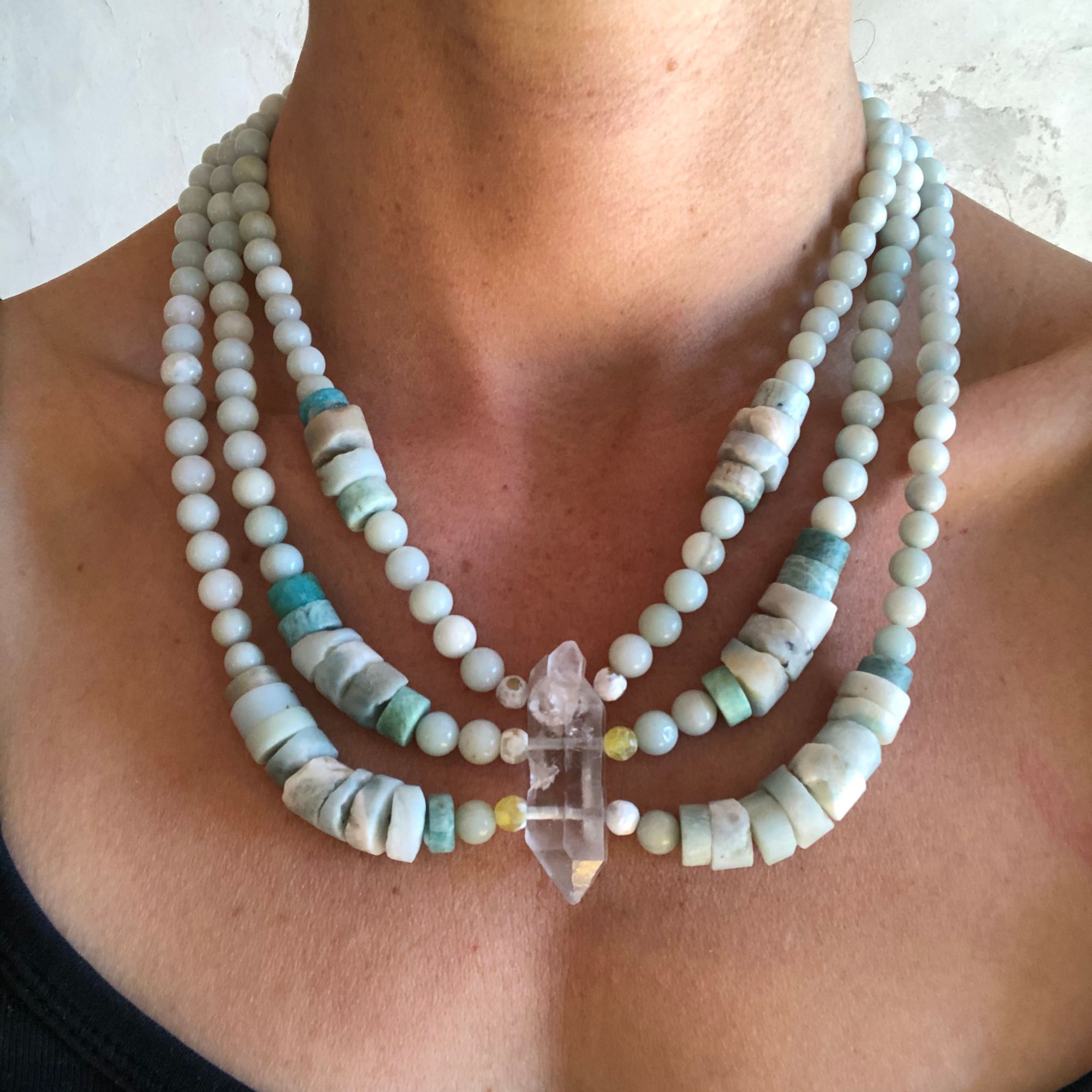 Woman wearing green-blue amazonite necklace with a double terminated quartz point laying on a flat, tan stone
