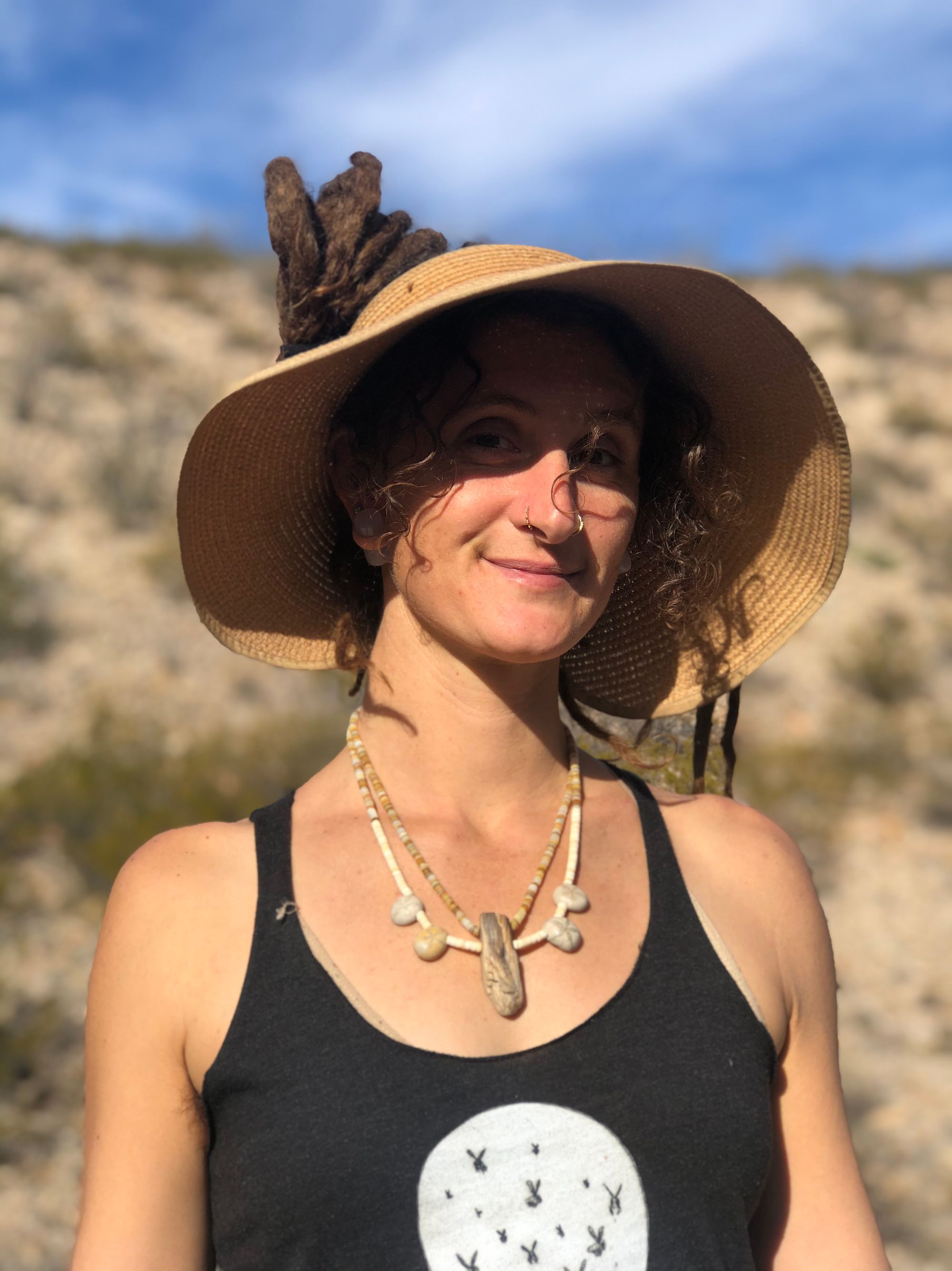 portrait of a woman in the desert wearing a hat and a necklace made of shell heishi, fossils and petrified wood