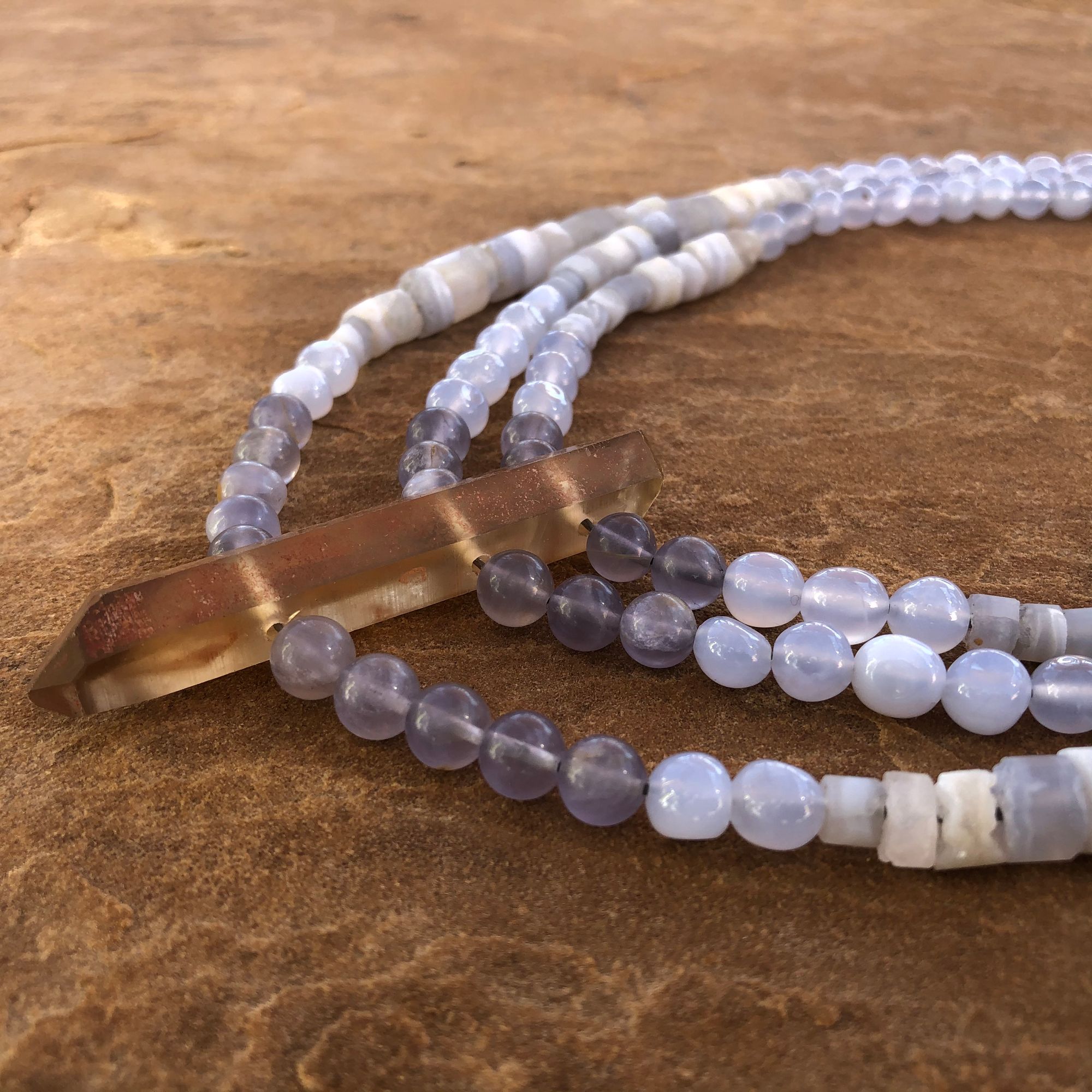 Blue chalcedony and golden Zambian citrine necklace laying flat on a tan stone