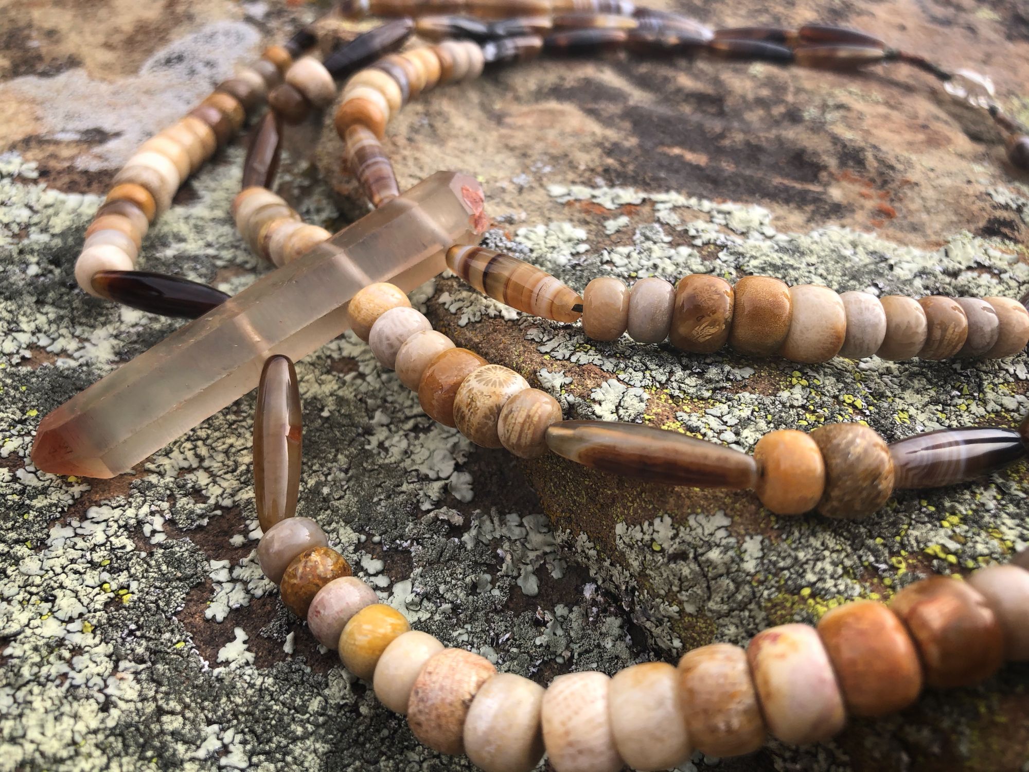 Brown necklace made with Zambian citrine, fossilized coral and picture agate laying on a stone covered in green lichen