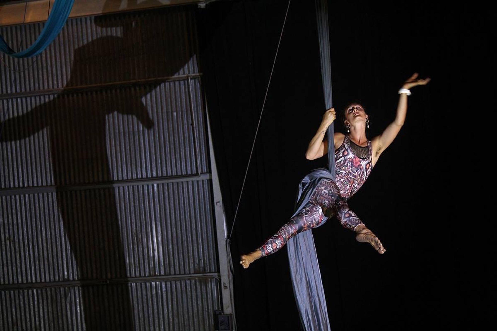 Woman wearing psychedelic print unitard doing aerial acrobatics on grey fabric in a metal warehouse