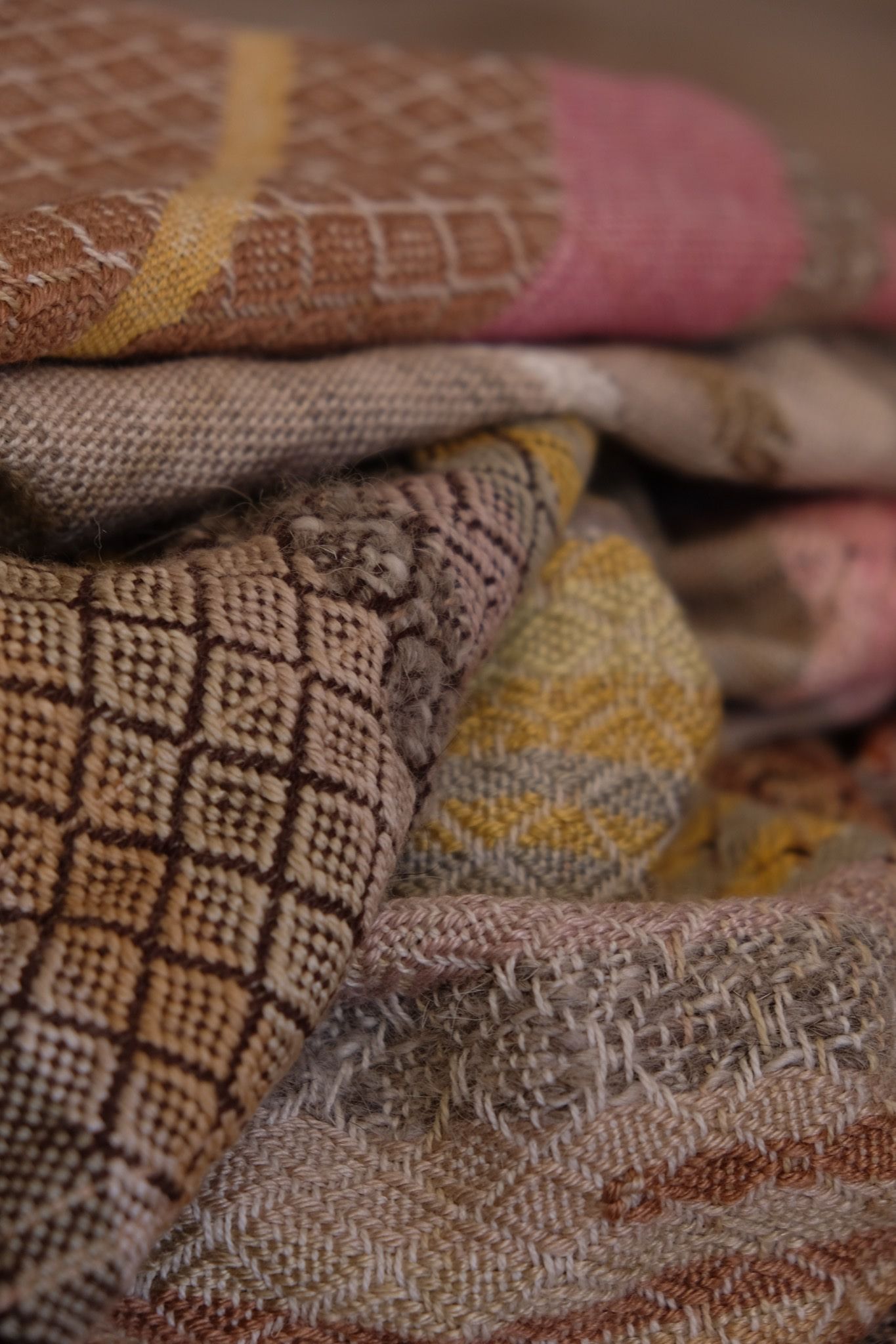 Detail of a handwoven pink, brown, tan, yellow and grey shawl with diamond pattern weave
