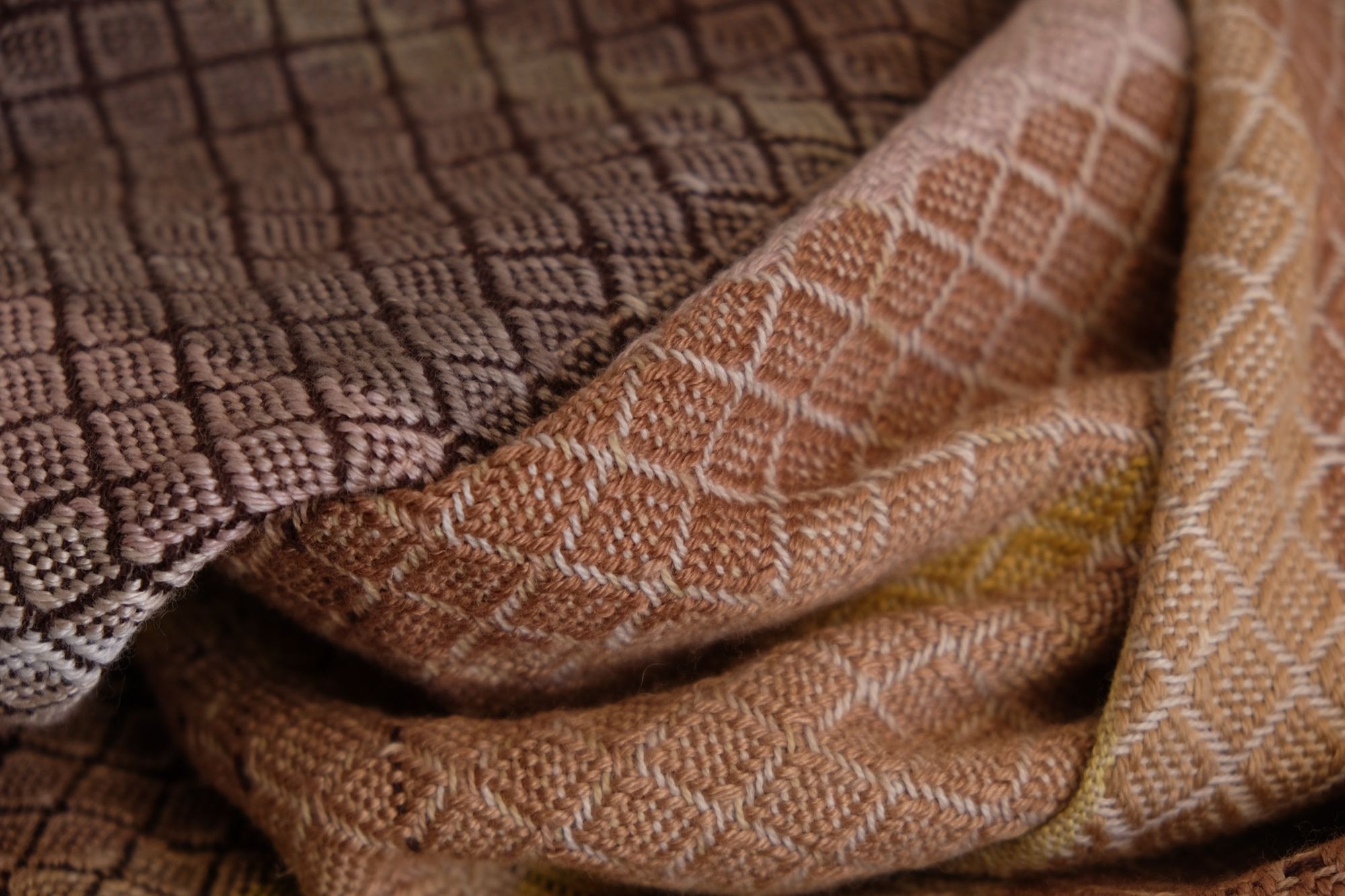 Detail of a handwoven pink, brown, tan, yellow and grey shawl with diamond pattern weave