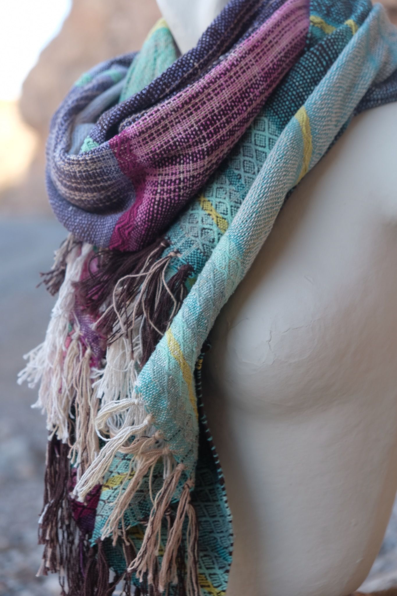 Blue, pink, yellow, purple and teal handwoven silk scarf on a white mannequin.