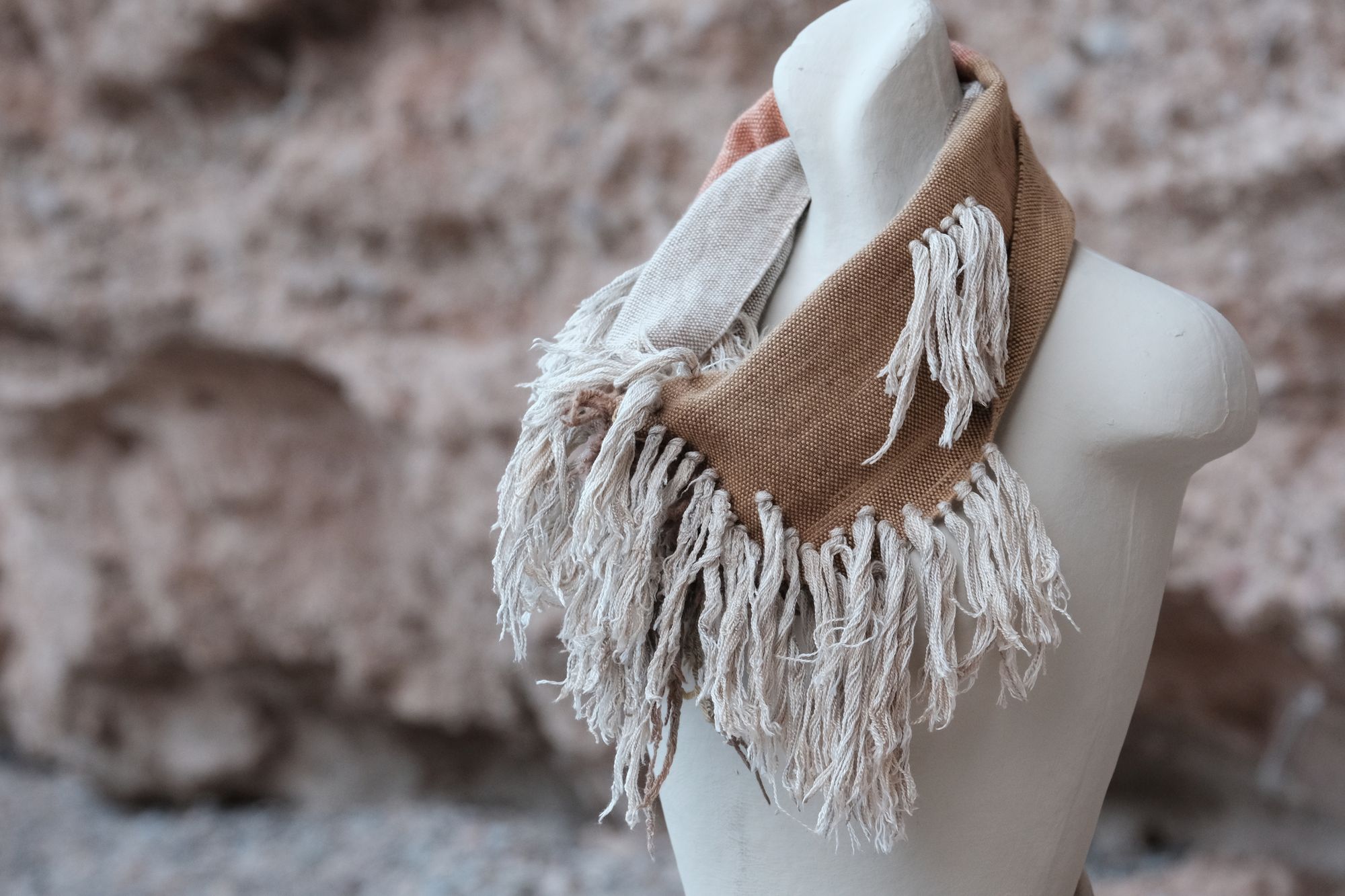 salmon colored, brown, white and grey scarf with white cashmere fringe on a white mannequin sitting on a tan rock