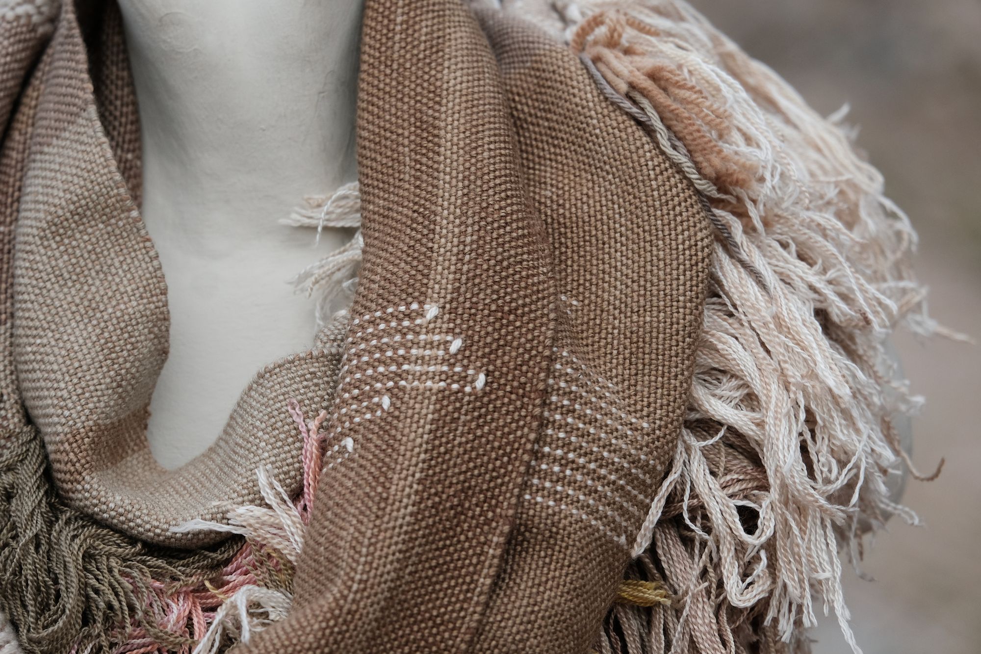 detail of Handwoven naturally dyed brown, grey, yellow, pink and green scarf with sumptuous sculptural fringe on a white mannequin on a rock in the desert