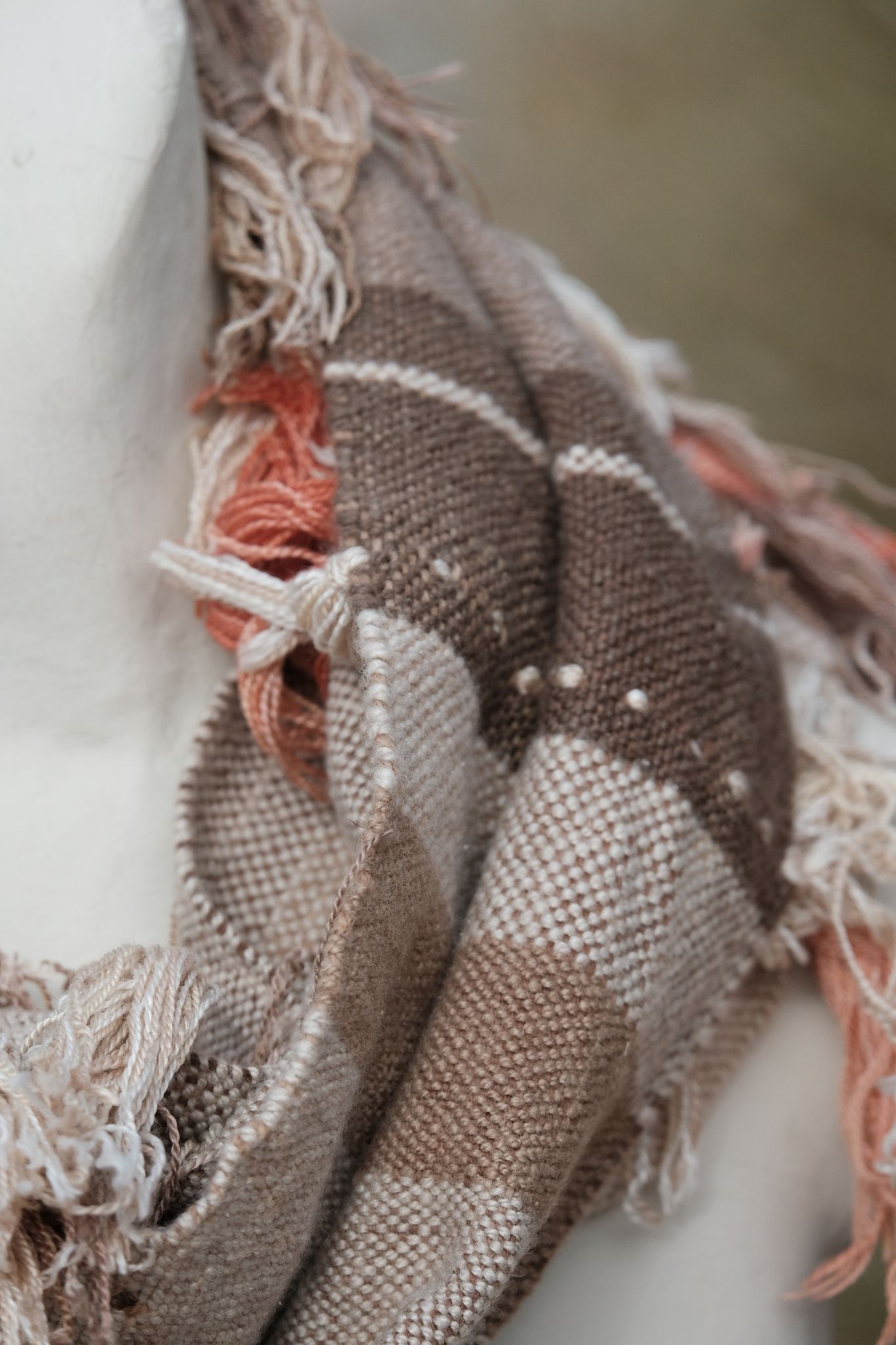 Detail of Grey and white handwoven cashmere scarf with naturally dyed salmon, brown and yellow fringe on a white mannequin sitting on a rock in the desert
