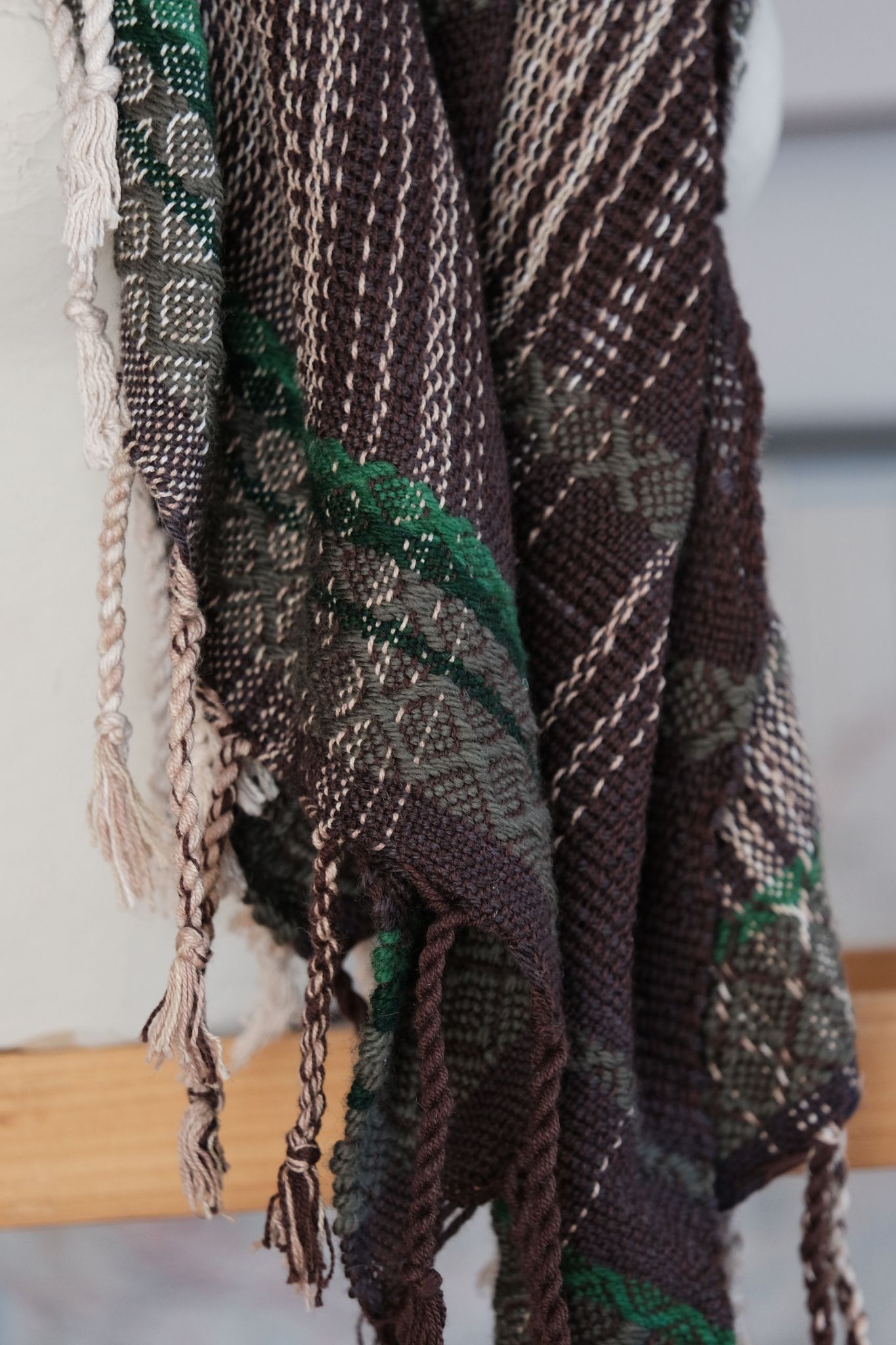 detail of handwoven wool and cotton scarf in green, gold and brown, on a white mannequin