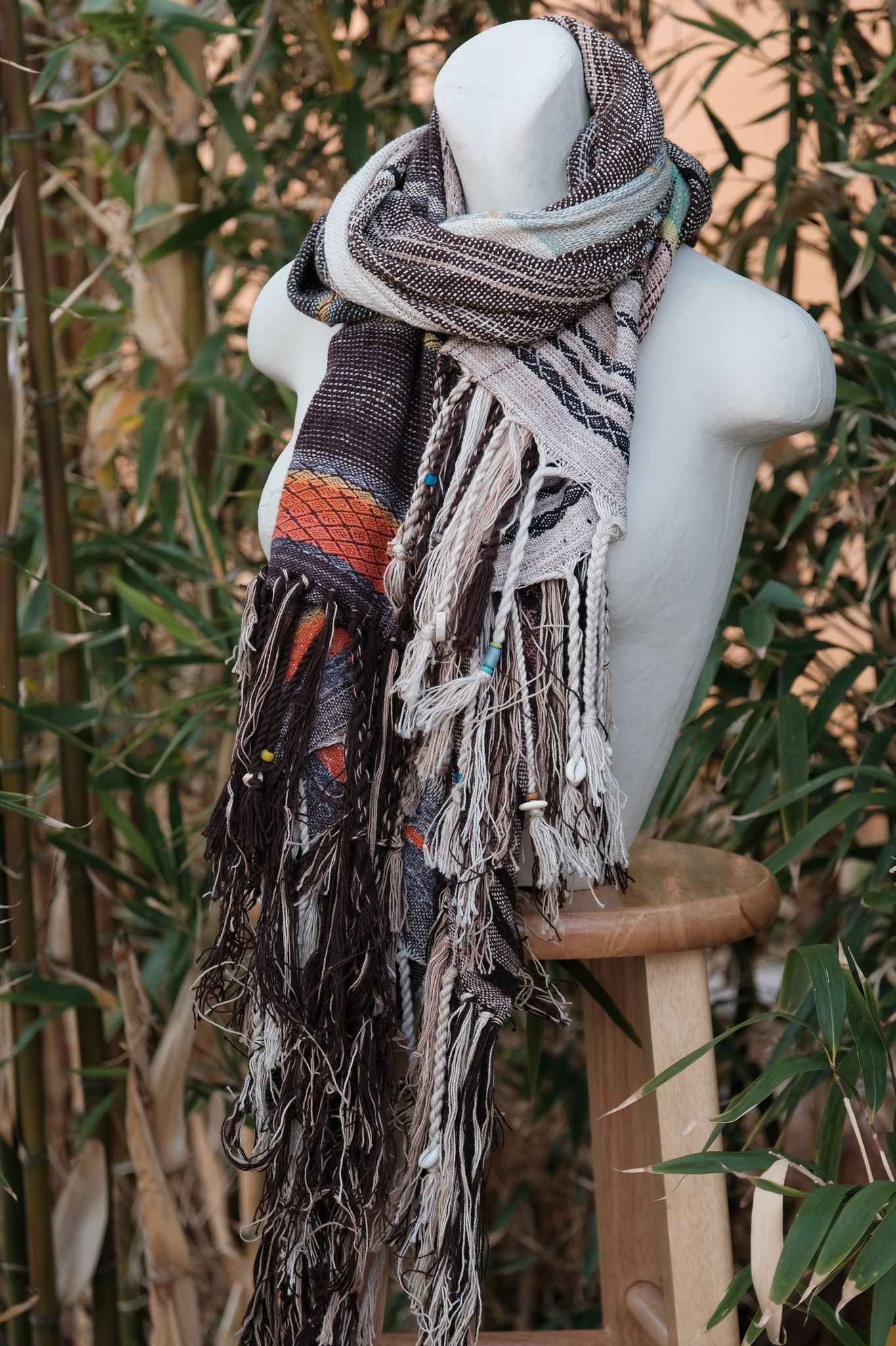 Handwoven raw silk etherial scarf in teal, blue, orange and dusty pink on a white mannequin in a garden