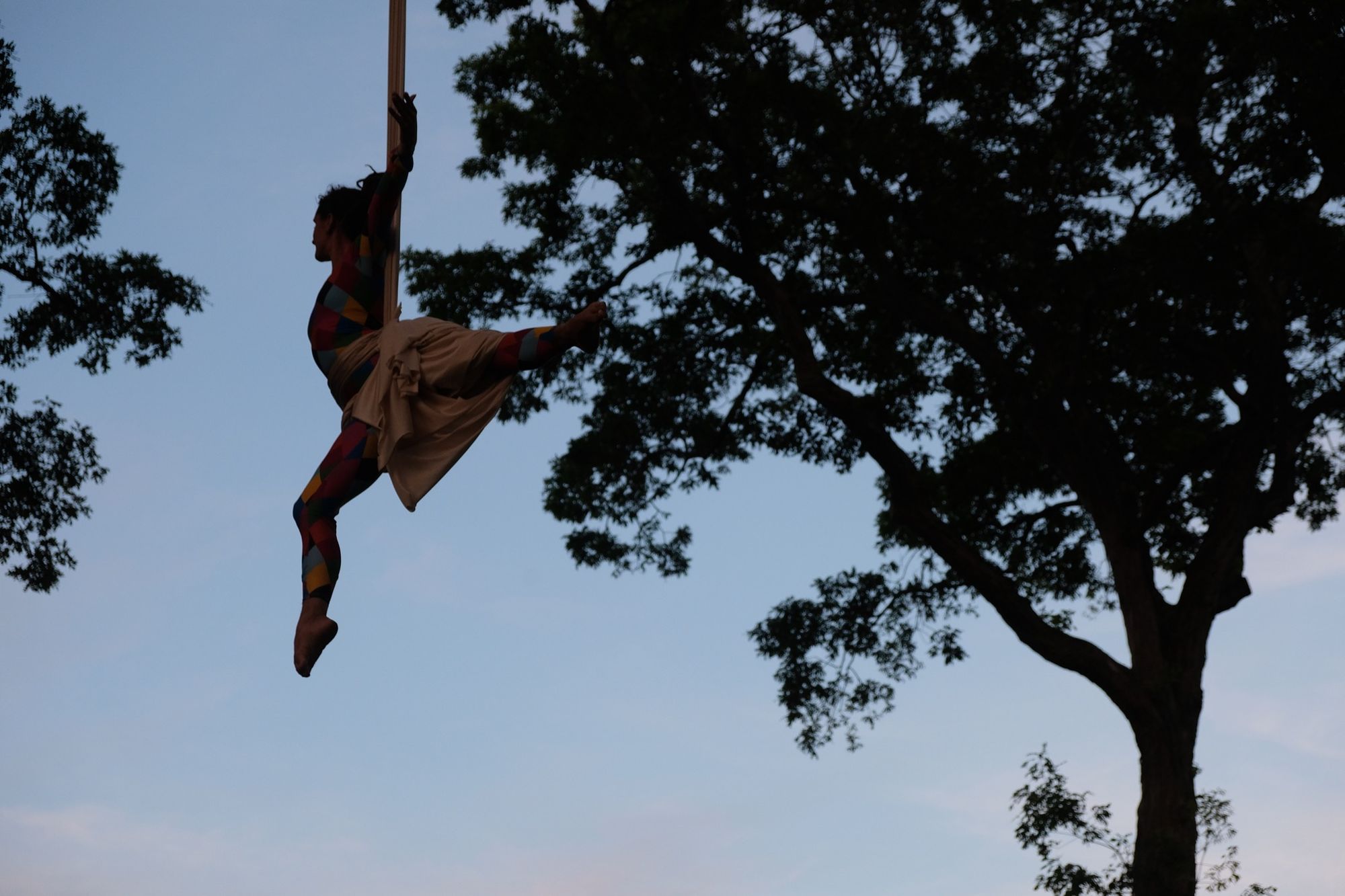 Woman doing aerial acrobatics with white fabric, hanging from a tree trimming bucket truck.