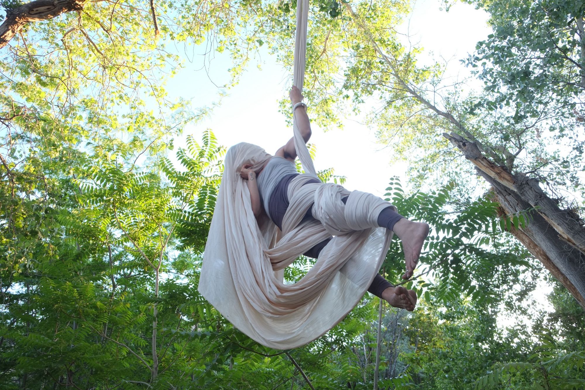 Woman doing aerial acrobatics with white fabric in the forest.