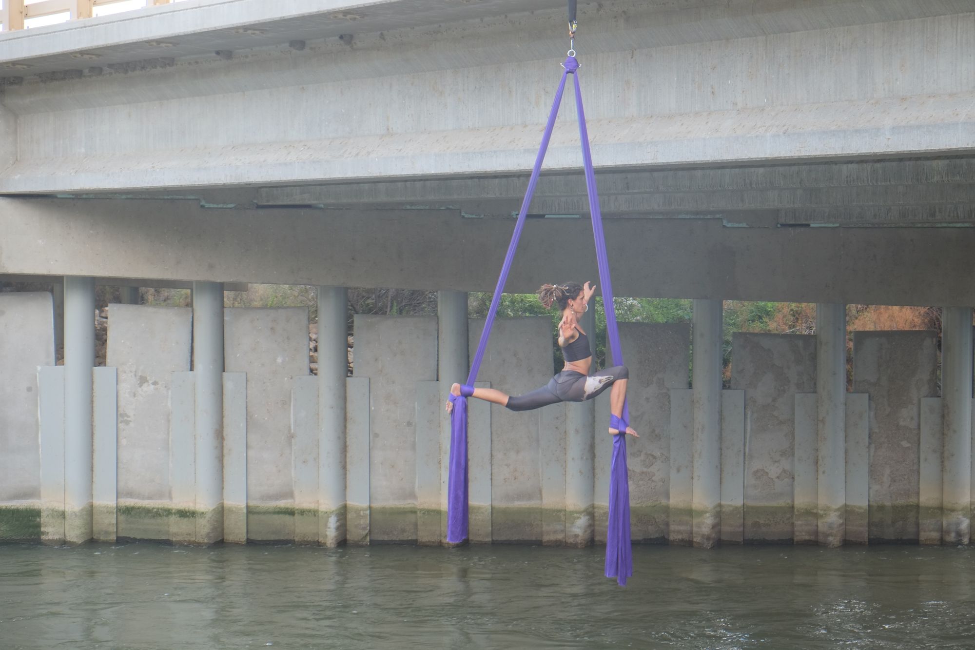 Woman doing aerial acrobatics with purple fabric, hanging from a bridge over the Rio Grande