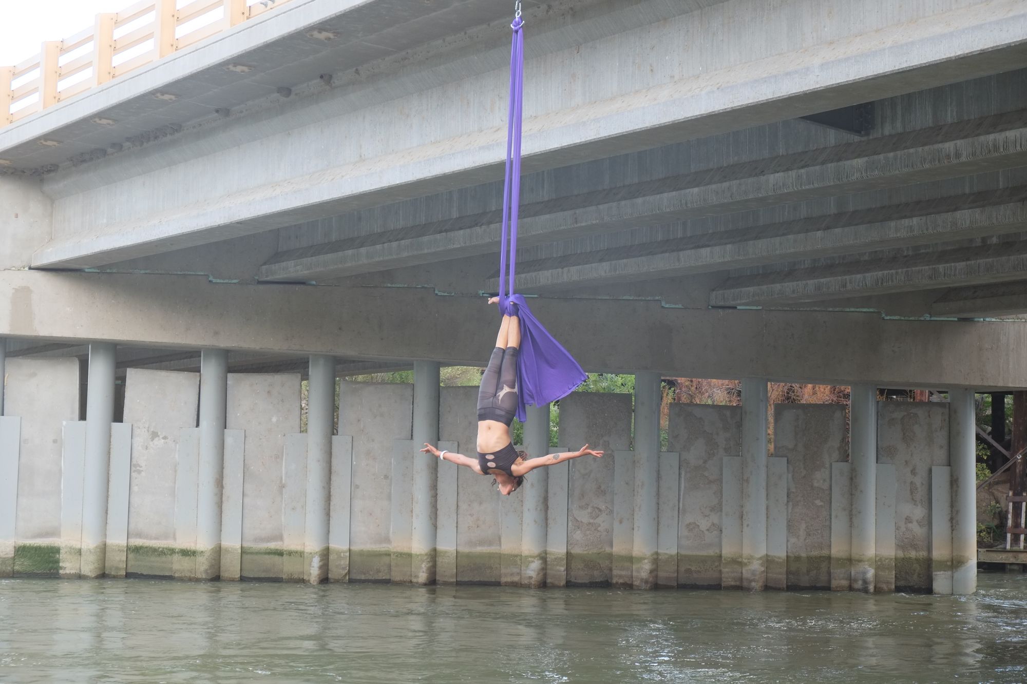 Woman doing hanging by her feet doing aerial acrobatics with purple fabric, hanging from a bridge over the Rio Grande