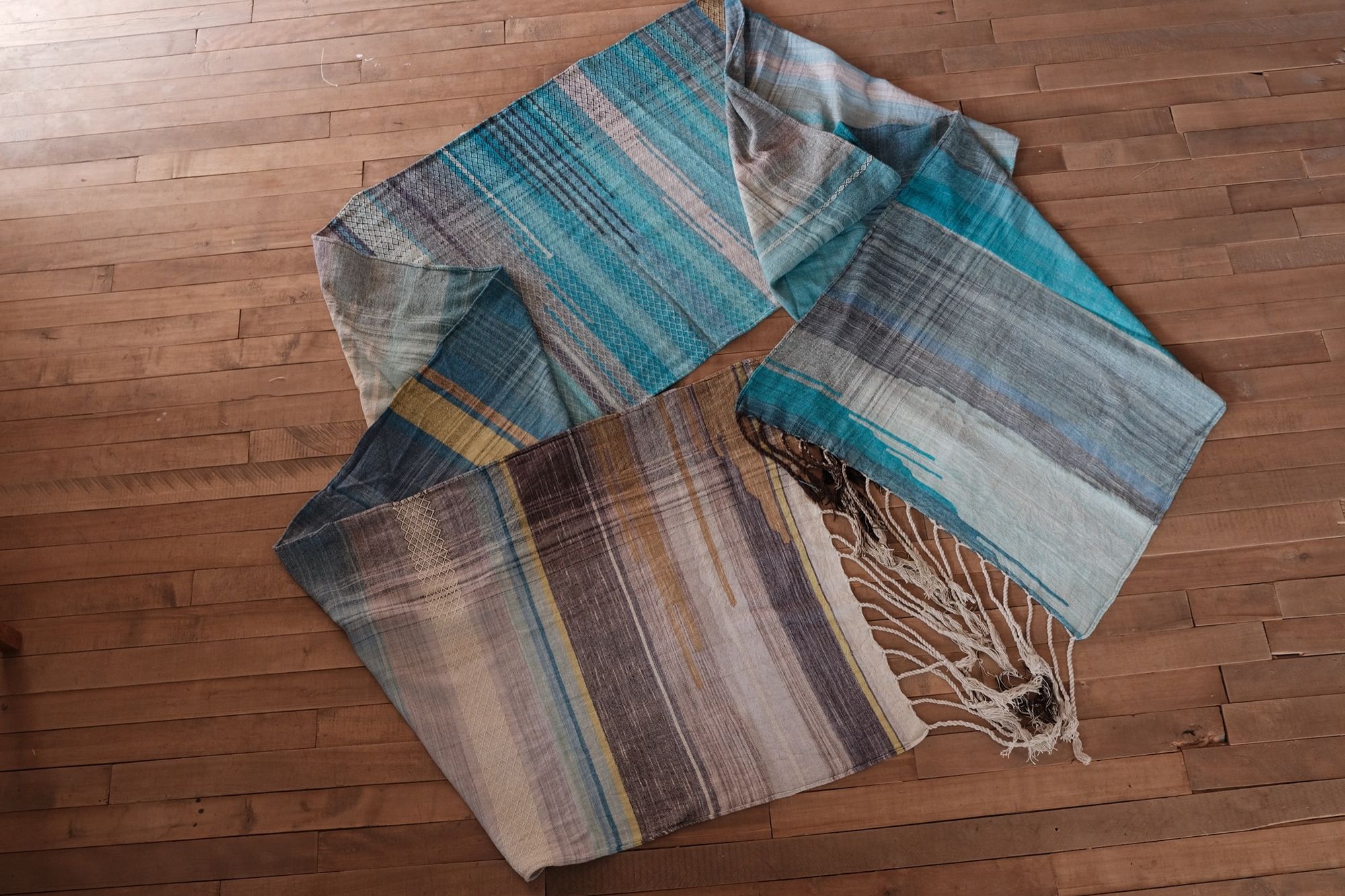 Handwoven fabric in all shades of blue, with details of white and golden yellow, laid out on a wood floor.