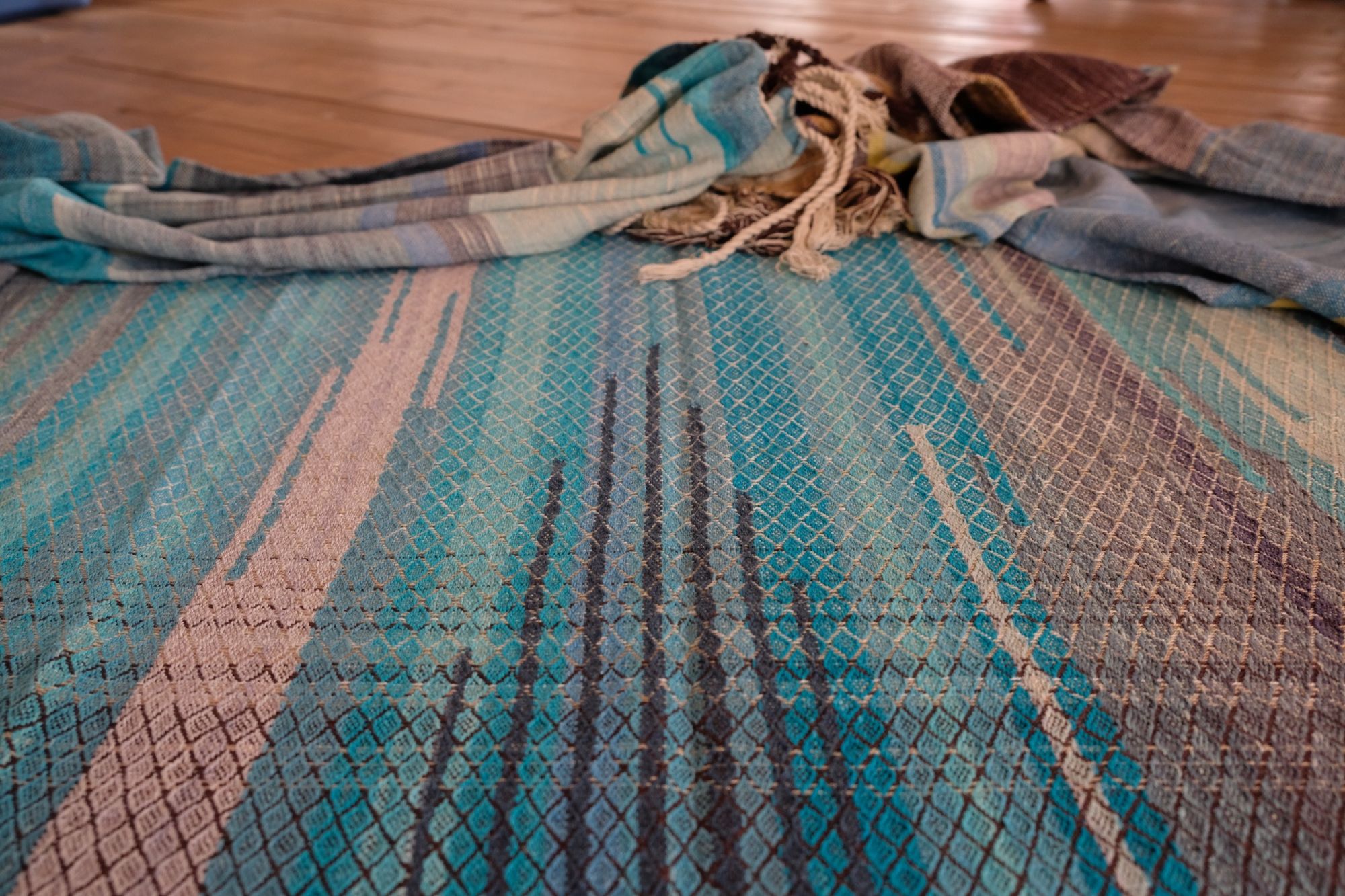 Handwoven fabric in all shades of blue, with details of white and golden yellow, laid out on a wood floor.