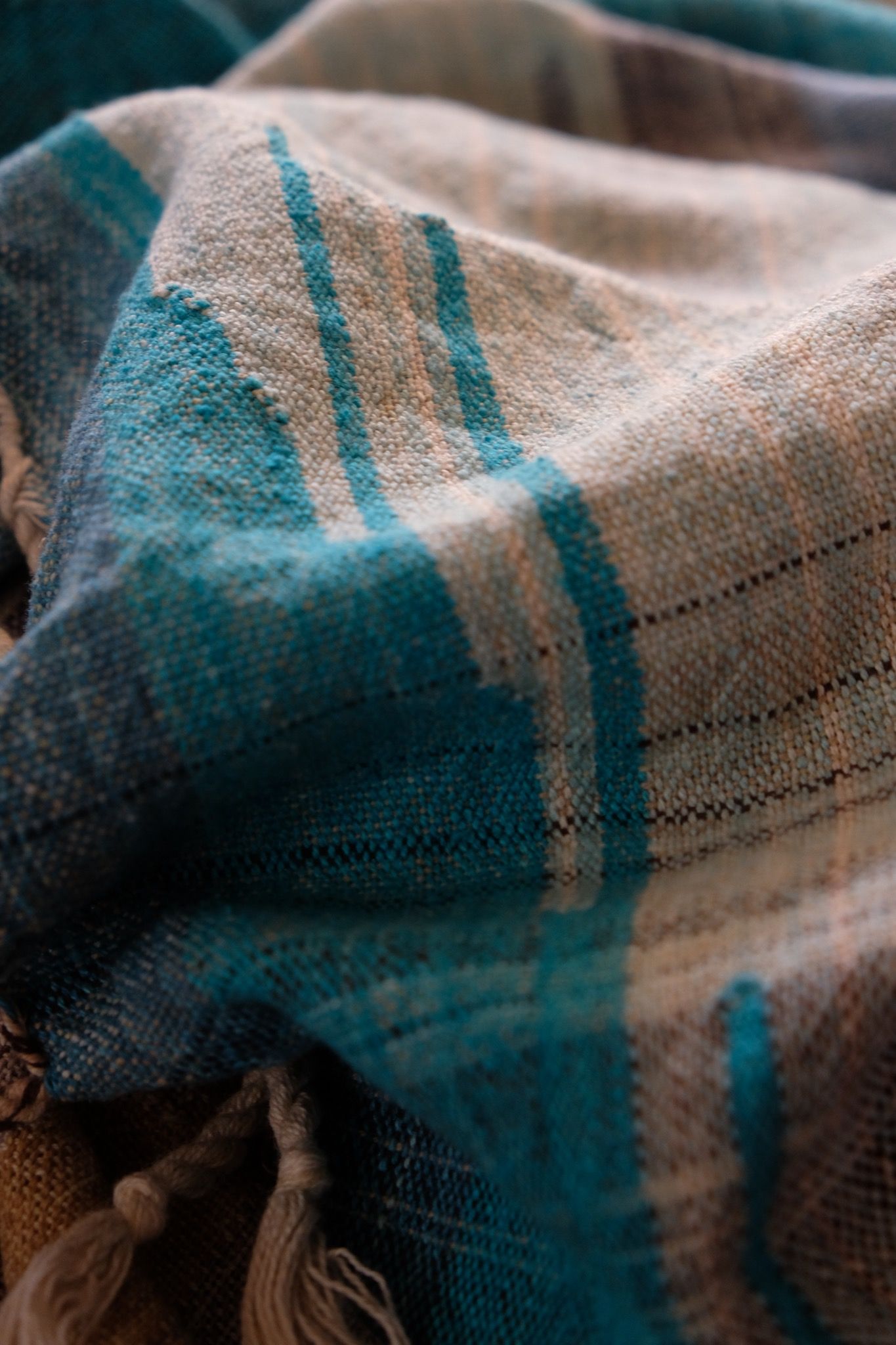 Details of Handwoven fabric in all shades of blue, with details of white and golden yellow, laid out on a wood floor.