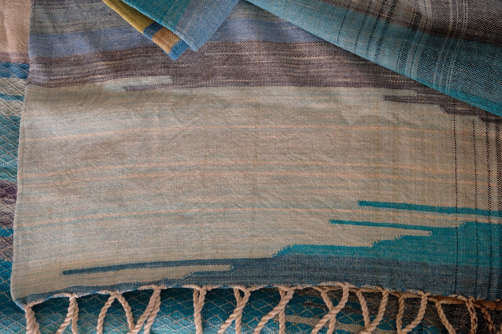 Details of Handwoven fabric in all shades of blue, with details of white and golden yellow, laid out on a wood floor.