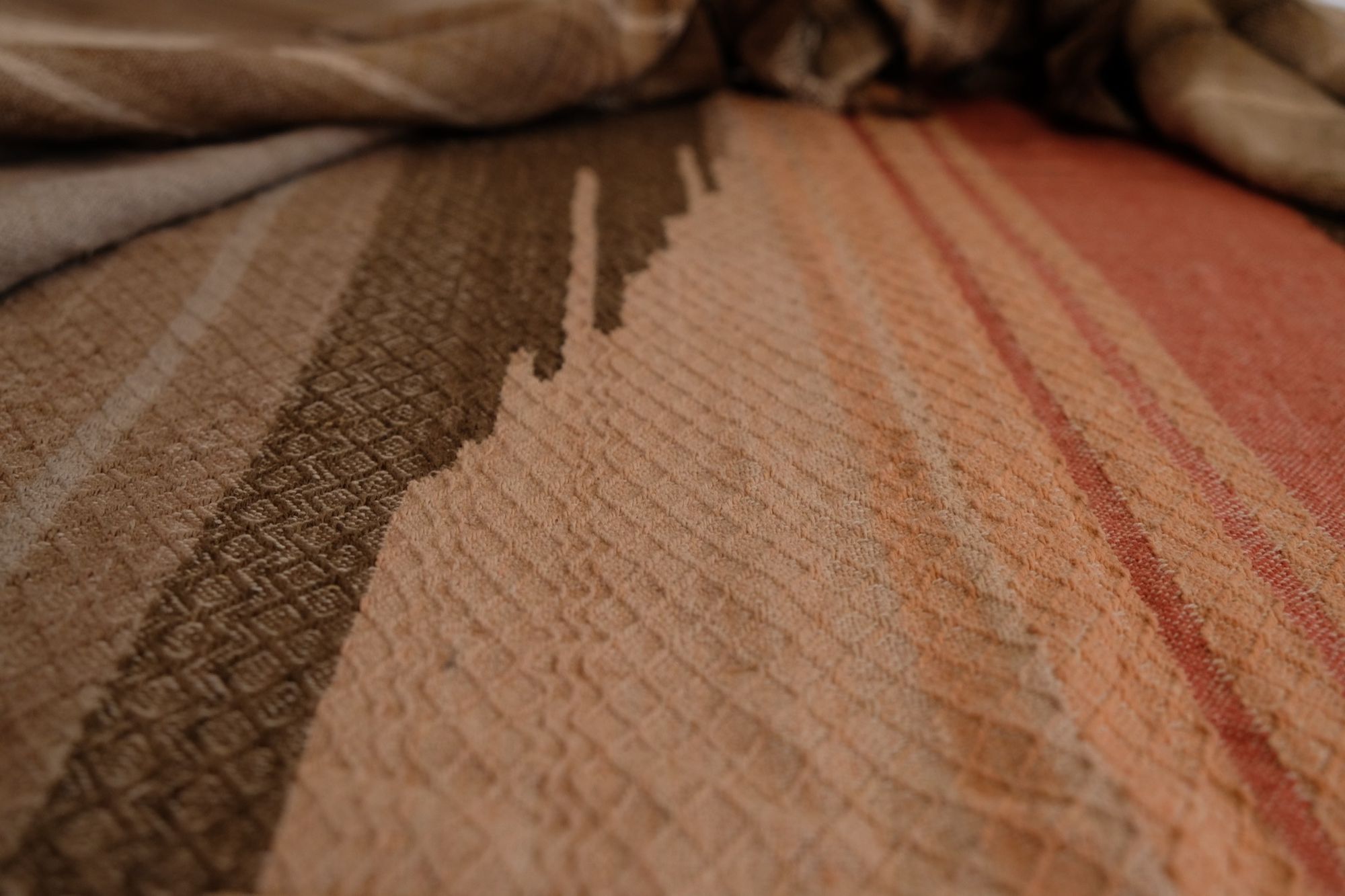 Detail of Handwoven shawl in brown, tan and salmon pink colors laying on a wood floor. 