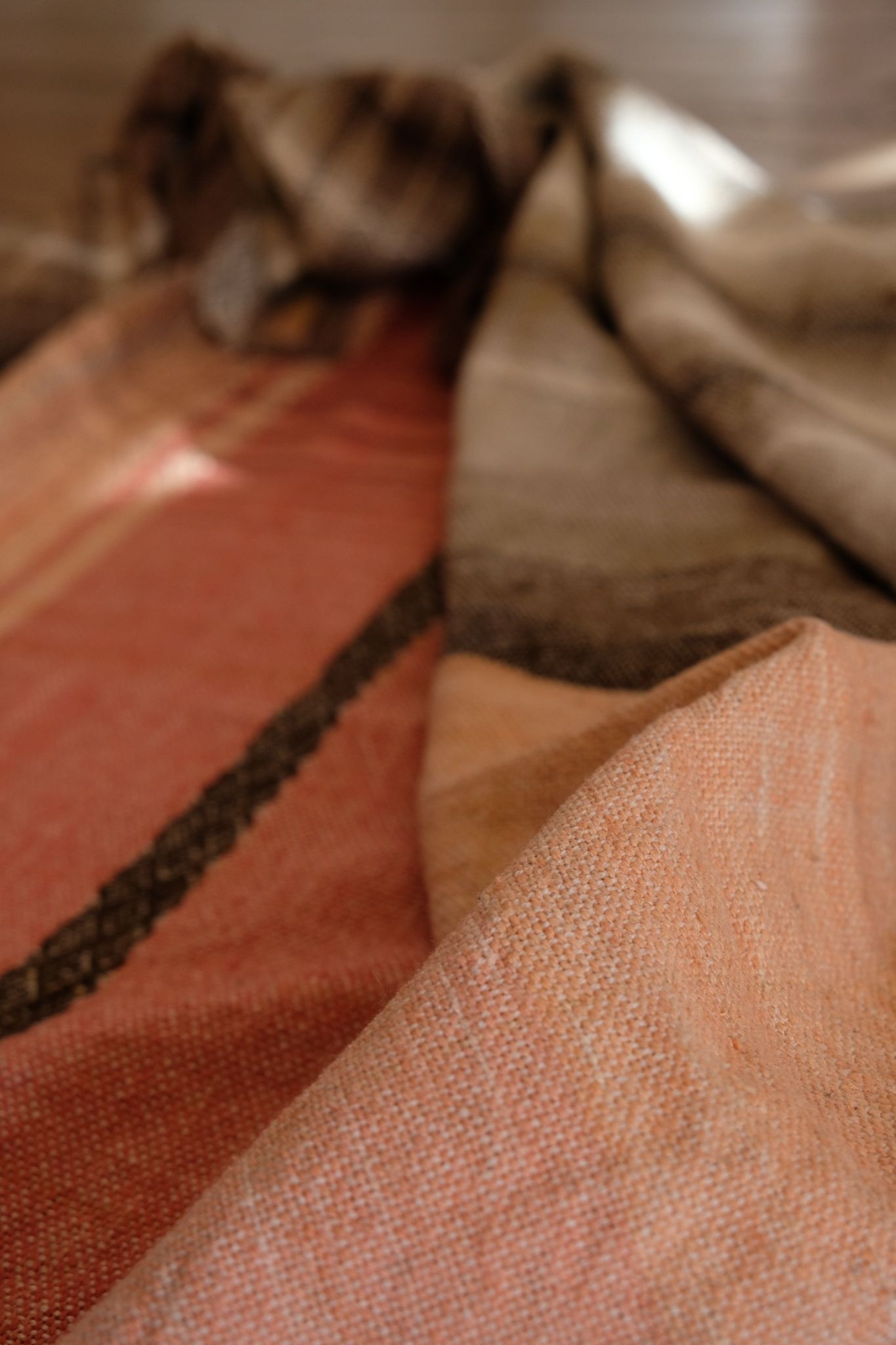 Detail of Handwoven shawl in brown, tan and salmon pink colors laying on a wood floor. 