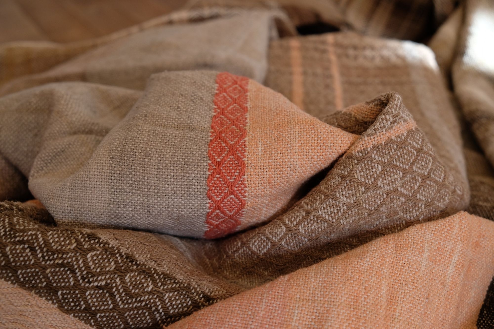 Detail of Handwoven shawl in brown, tan and salmon pink colors laying on a wood floor. 