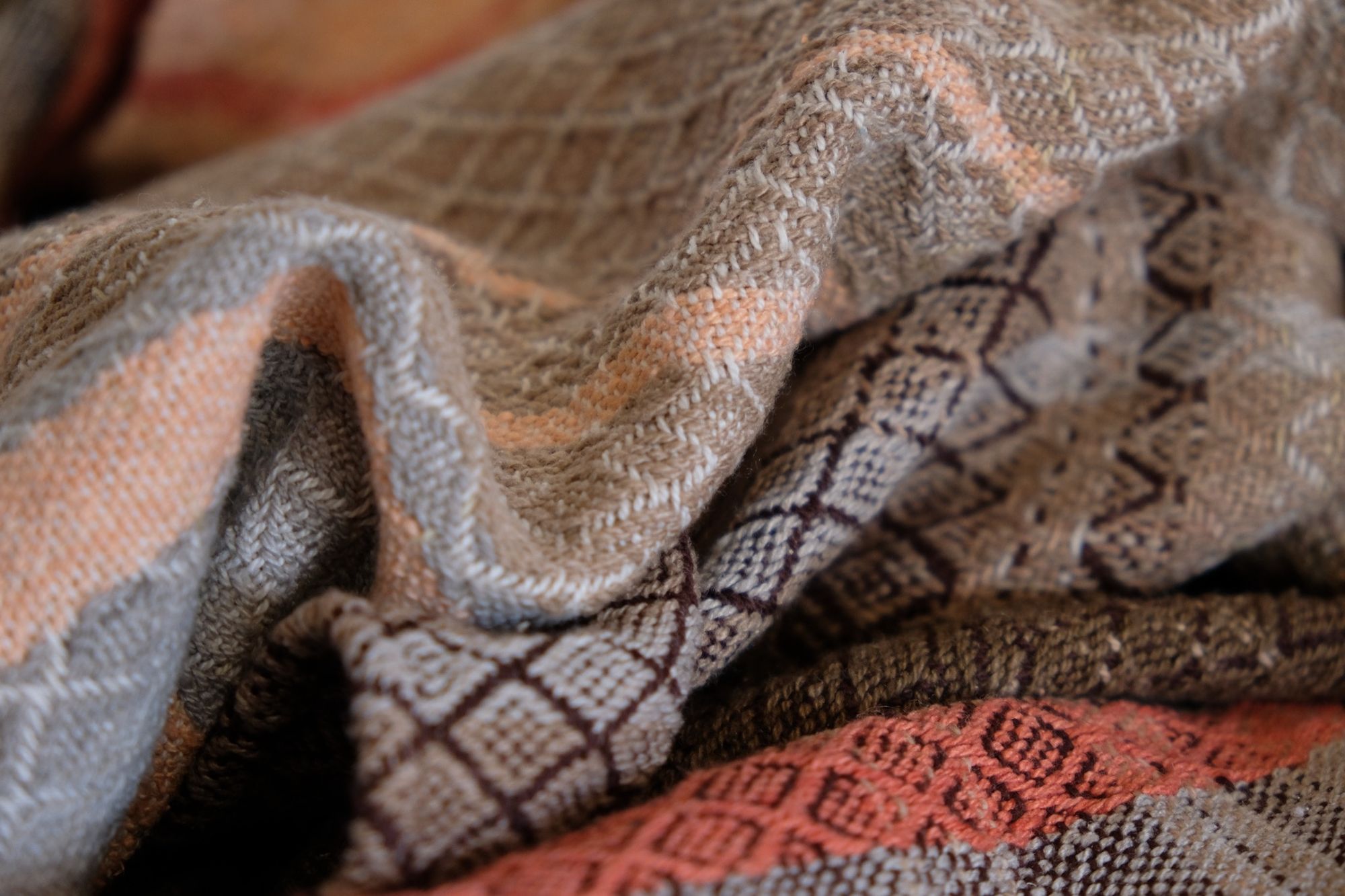 Detail of Handwoven shawl in brown, tan and salmon pink colors laying on a wood floor. 