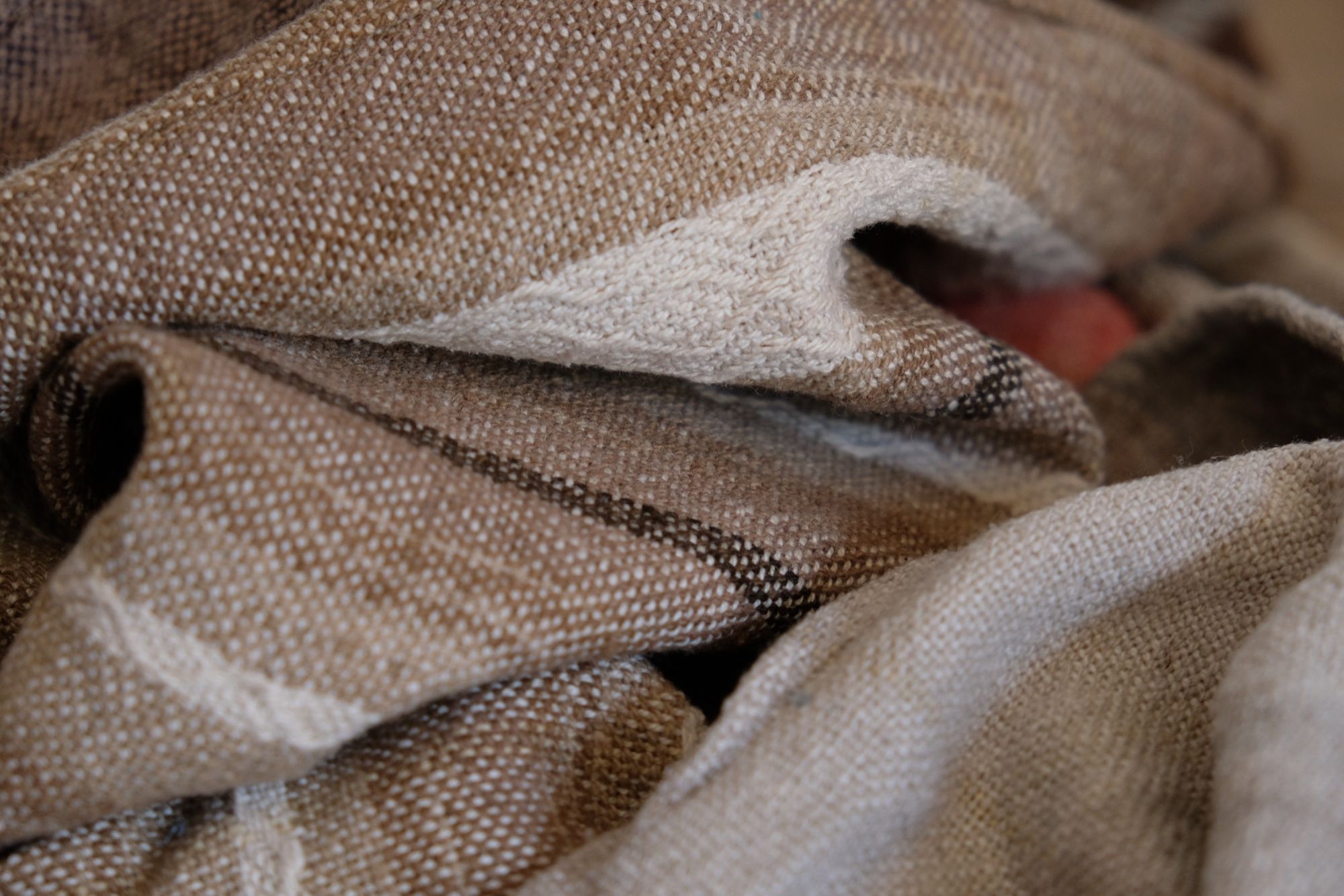 Detail of Handwoven shawl in brown, tan and salmon pink colors laying on a wood floor. 