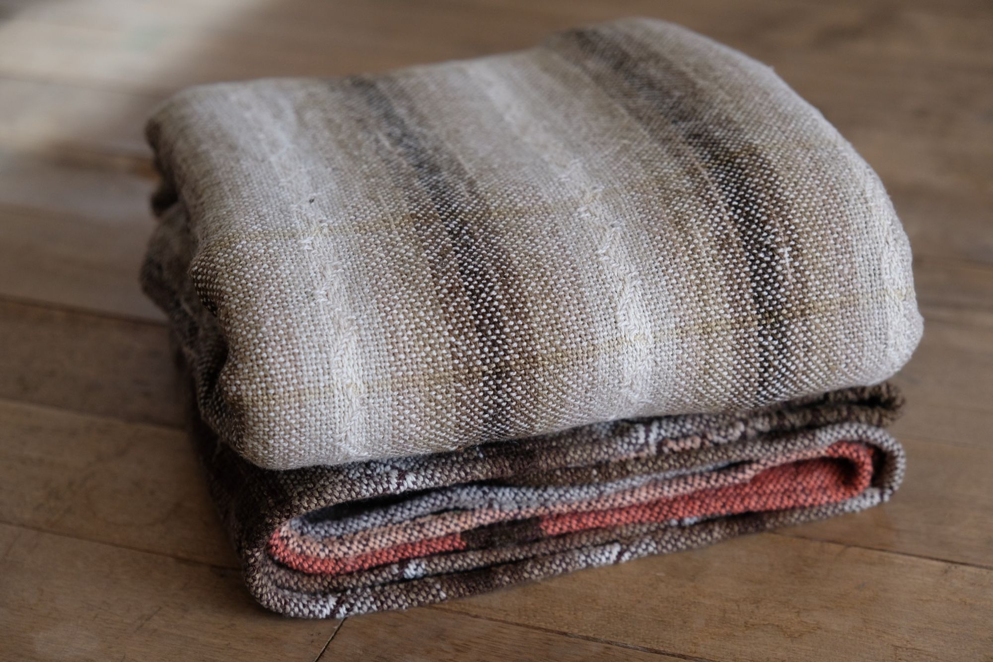 Detail of Handwoven shawl in brown, tan and salmon pink colors laying on a wood floor. 