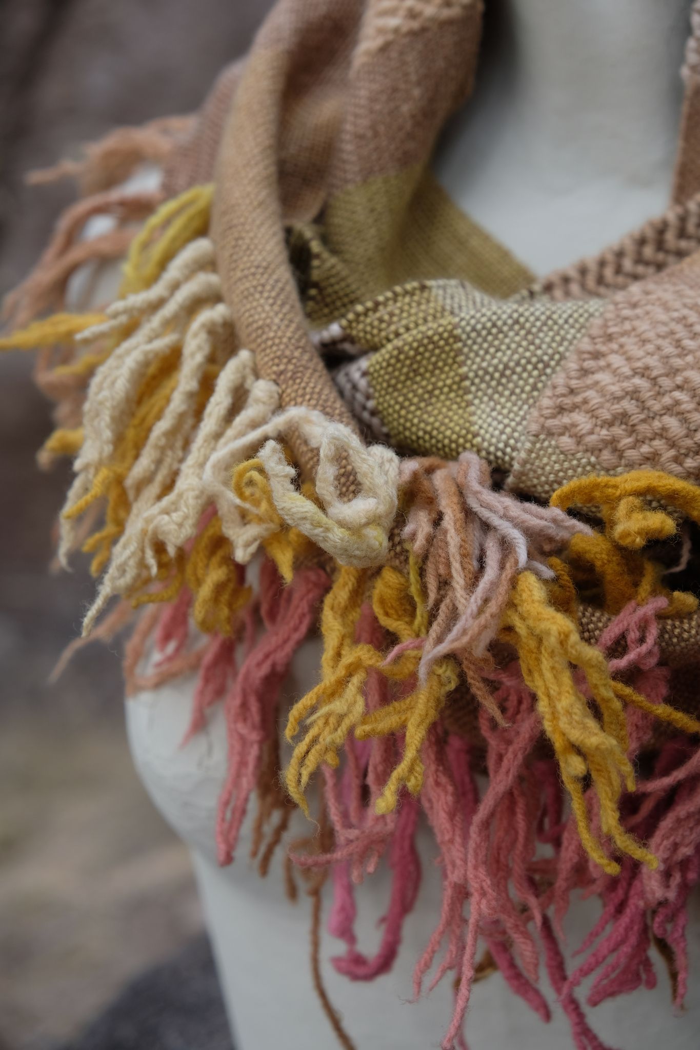 naturally dyed brown, pink, yellow, tan and red merino scarf with fringe on a white mannequin