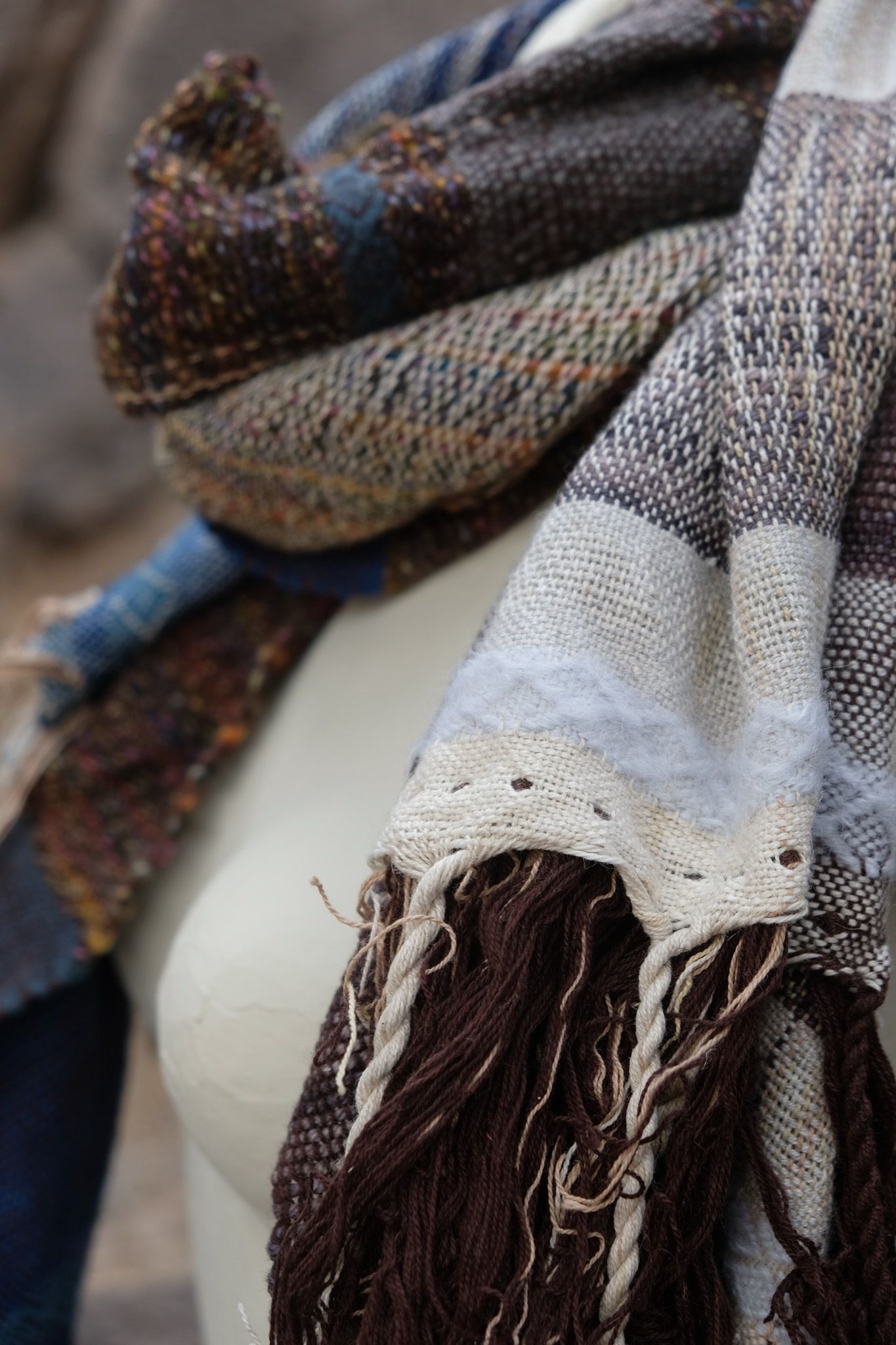 detail of Blue, white and brown handwoven scarf on a white mannequin sitting on a boulder.