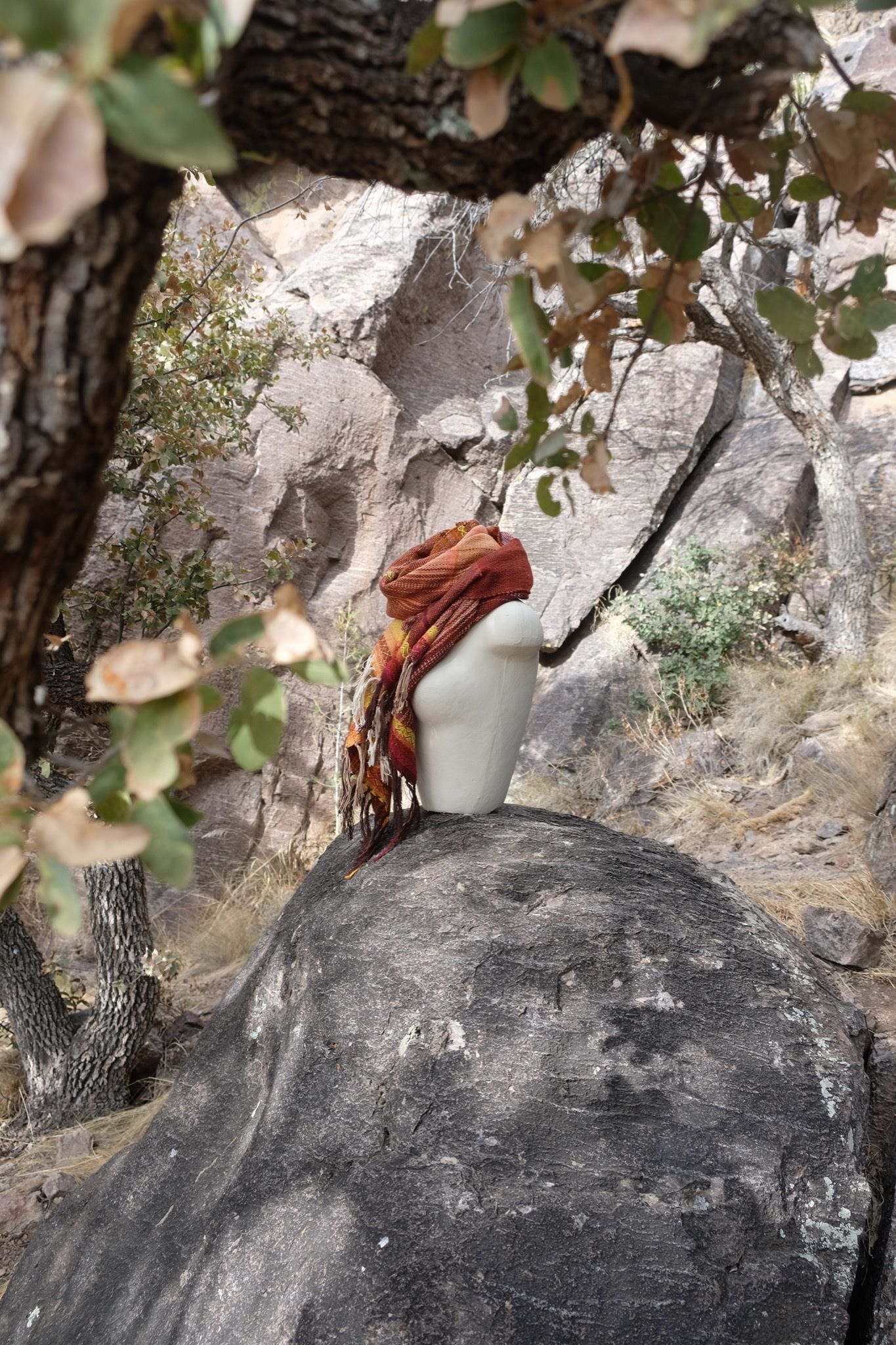 Handwoven red, orange, yellow, brown and white Merino Etherial Scarf on a white mannequin sitting on a boulder