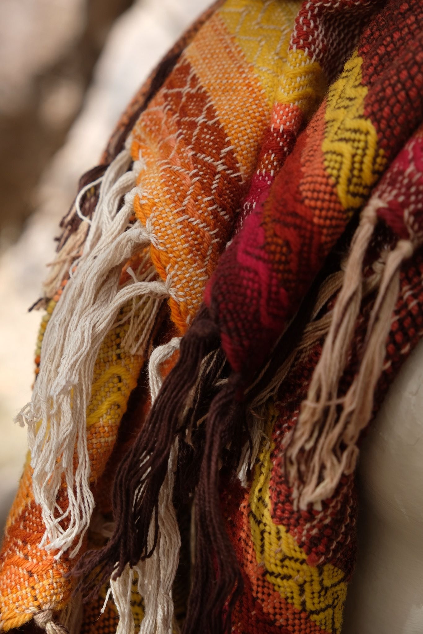 detail of Handwoven red, orange, yellow, brown and white Merino Etherial Scarf on a white mannequin sitting on a boulder