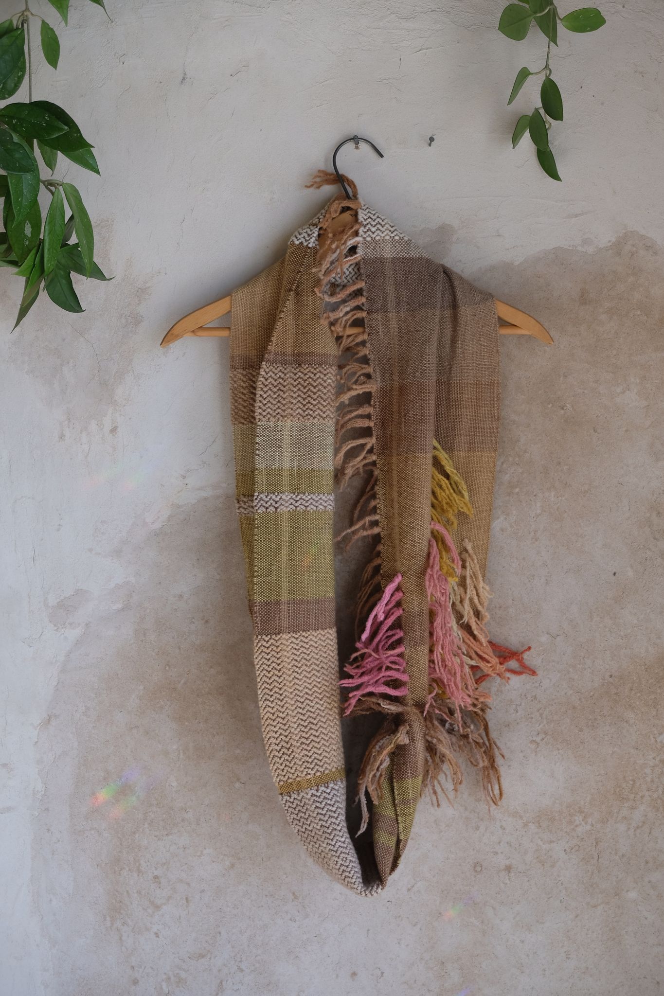 naturally dyed brown, pink, yellow, tan and red merino scarf with fringe on a hanger