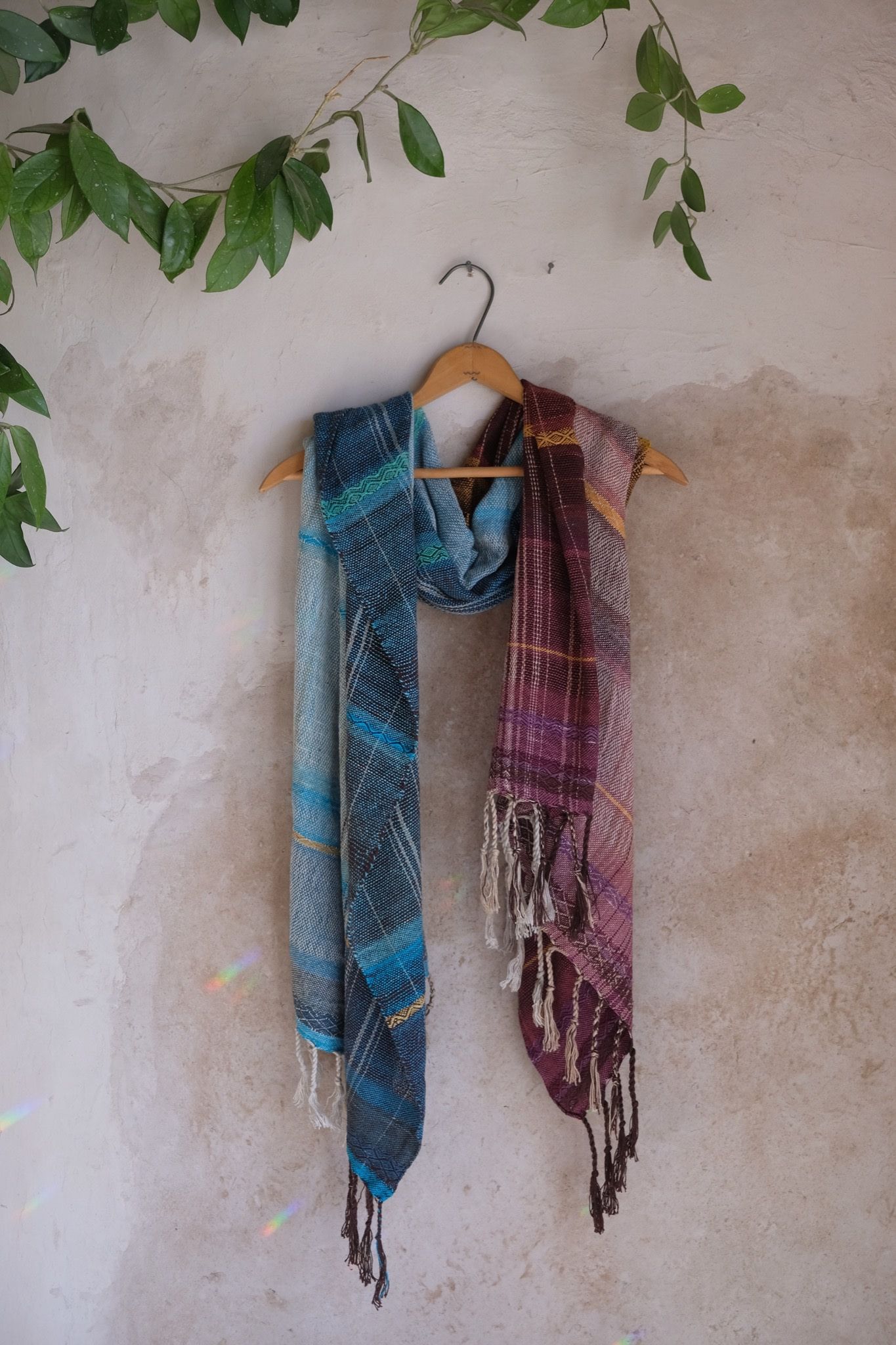 Handwoven maroon, blue, purple and yellow scarf on a hanger, hanging on a tan mud wall
