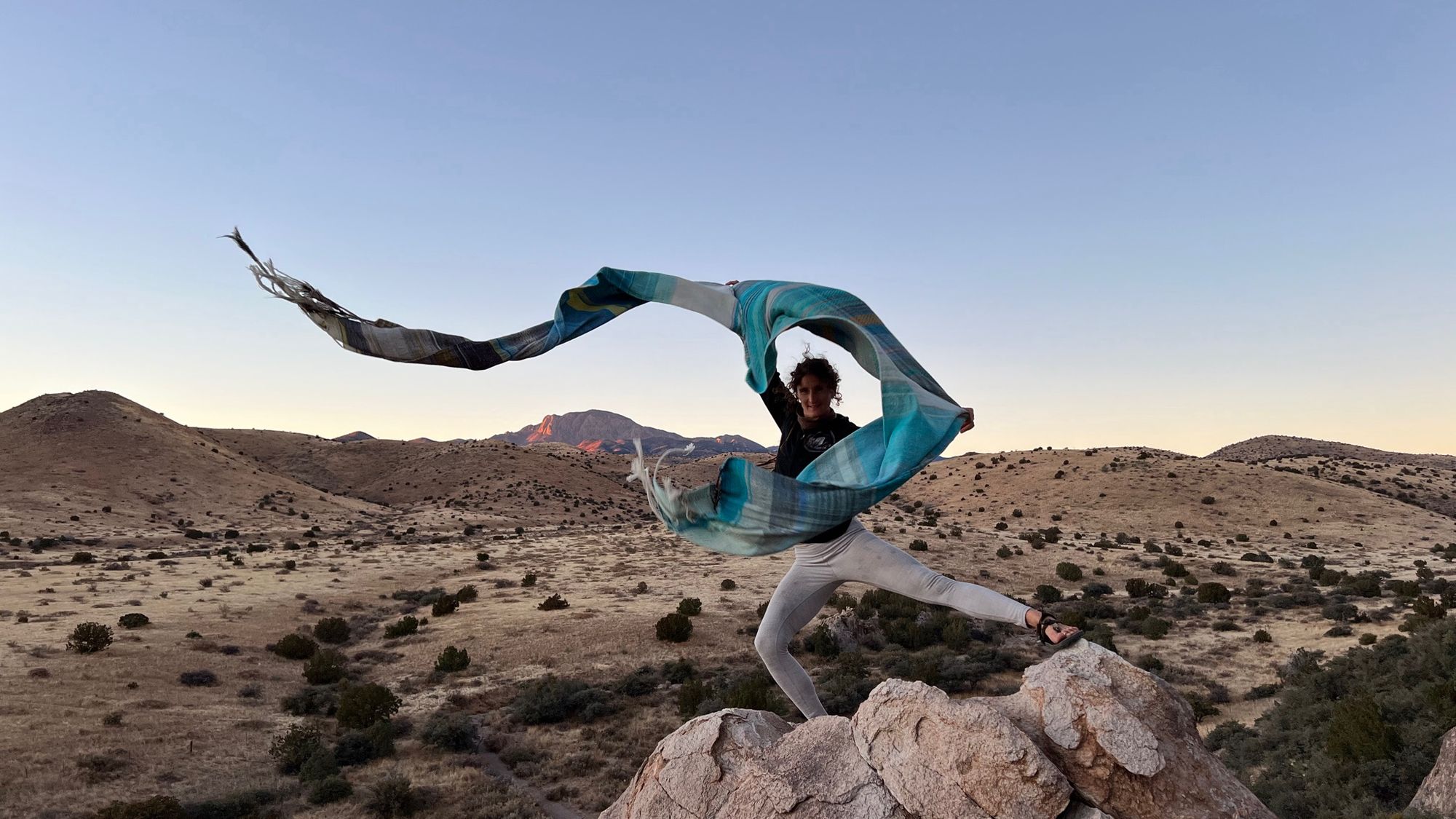 Woman in a mountain desert landscape dancing with a blue piece of handwoven fabric 