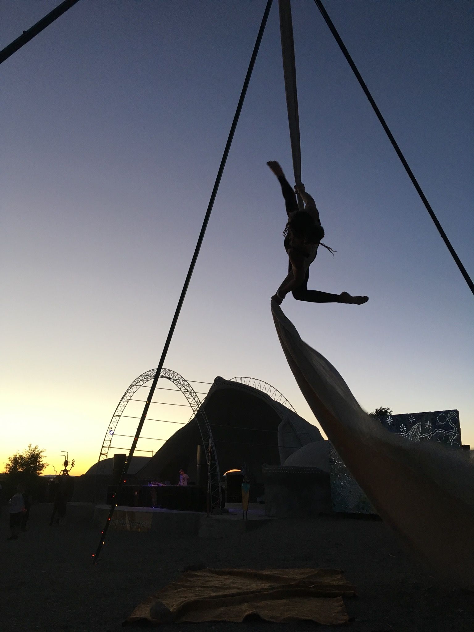 Woman doing aerial silks at a festival at sunset wit a dome covered stage. 