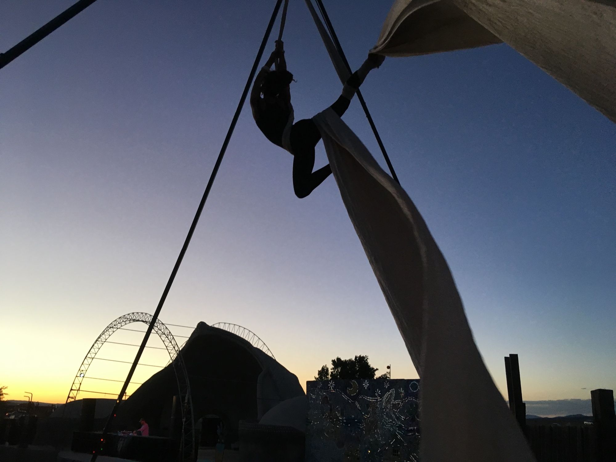 Woman doing aerial silks at a festival at sunset wit a dome covered stage in the background. 