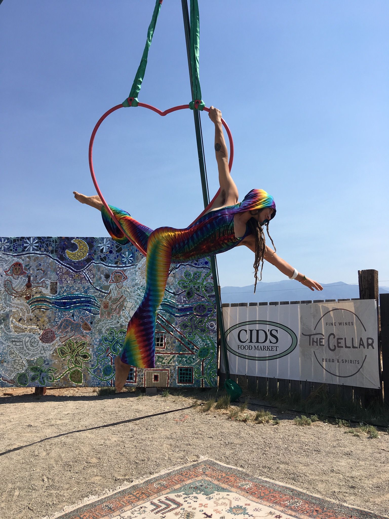 Woman in rainbow tie dye unitard doing acrobatics on an aerial heart