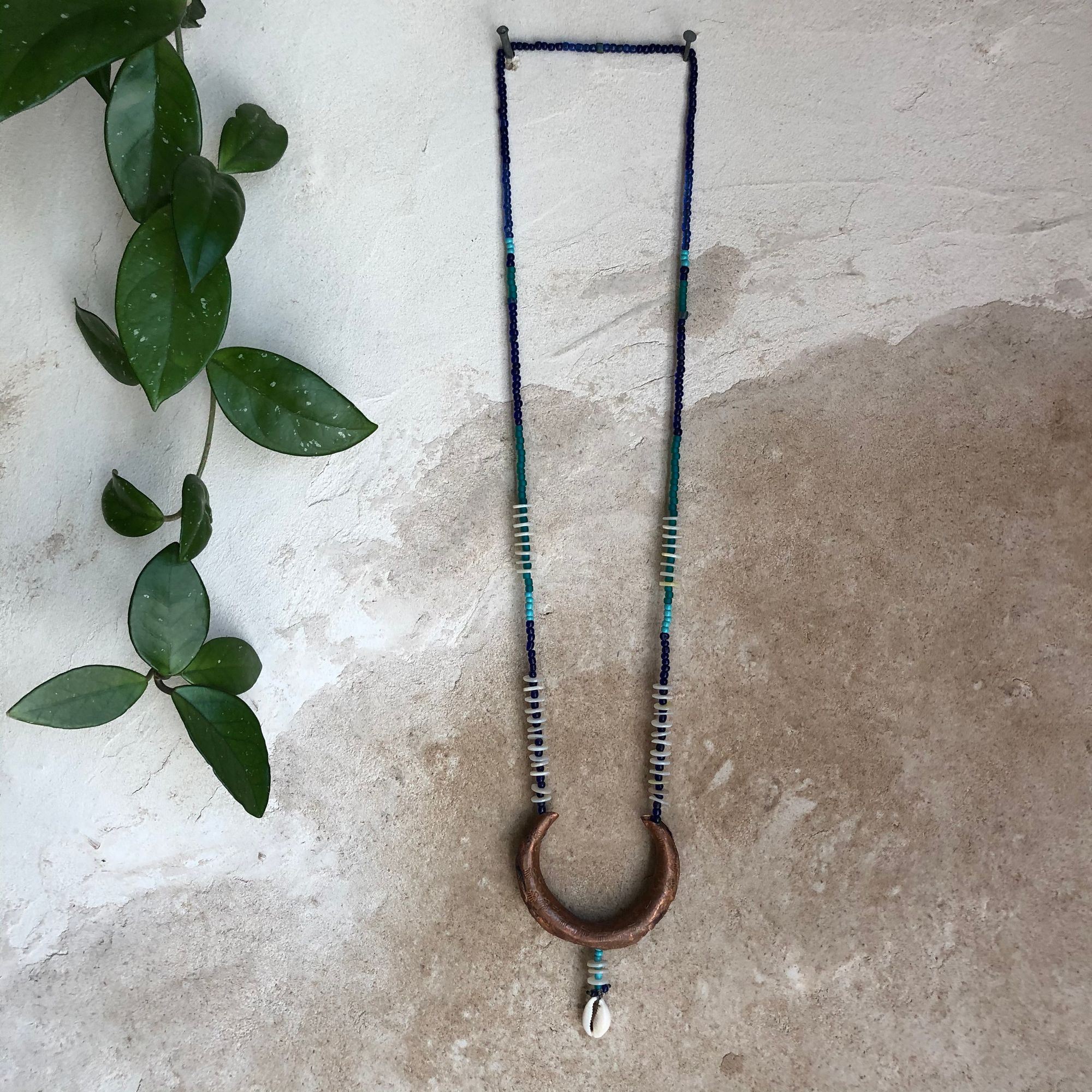  copper crescent moon necklace with blue beads hanging on a wall