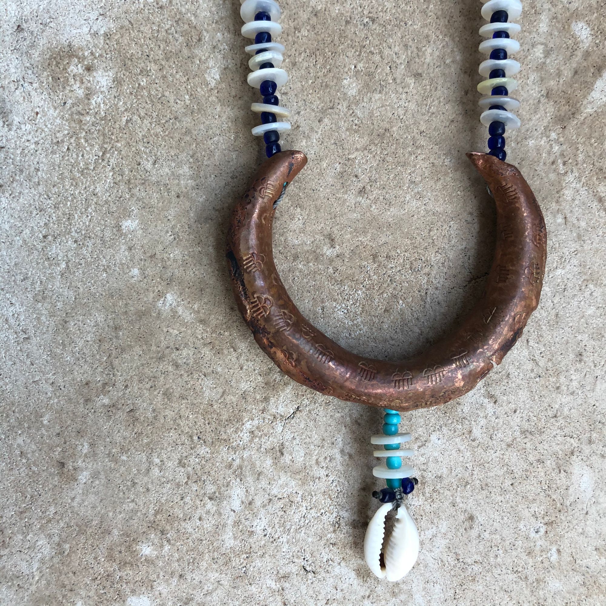 Detail of a copper crescent moon necklace with blue beads