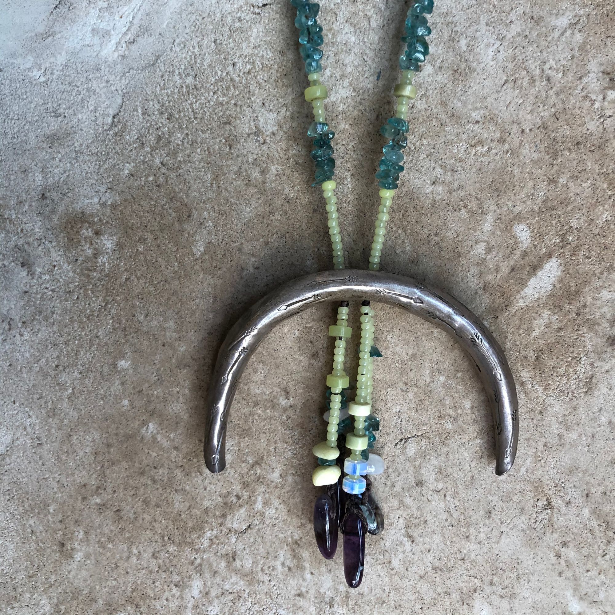 detail of  silver crescent moon necklace with green and purple beads hanging on a wall