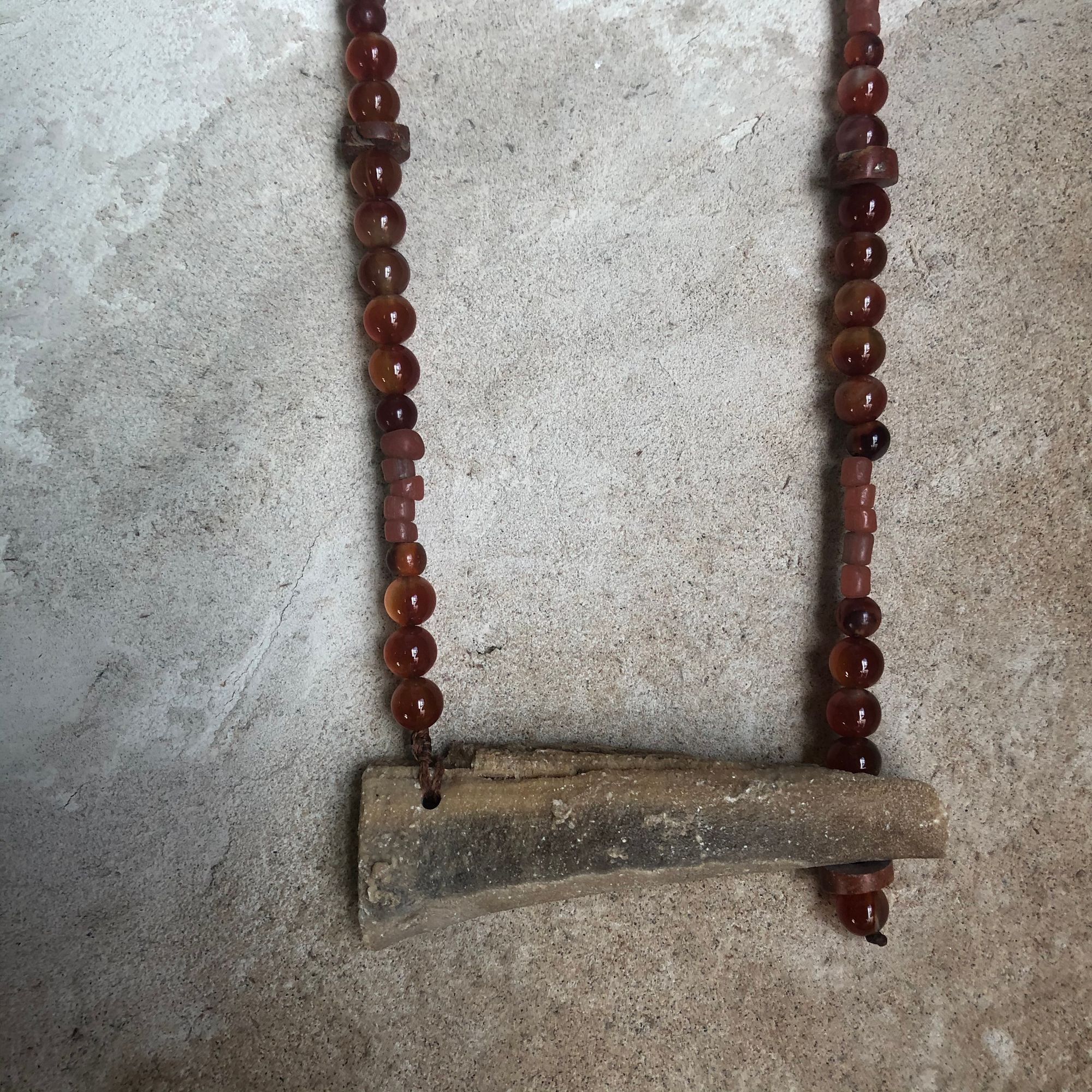 Necklace made of Stalaktit & red Carnelian, glass and bauxite beads hanging on a wall 