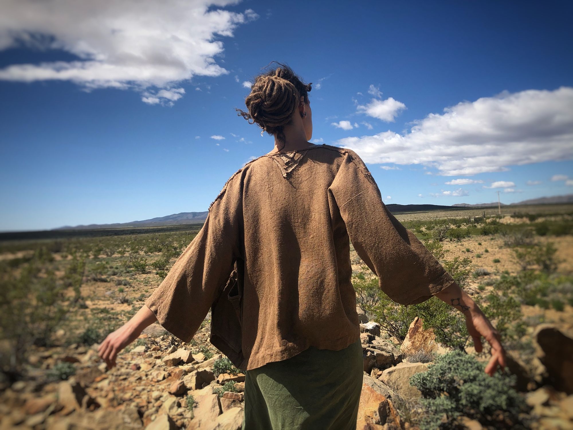 woman wearing handmade brown jacket and green skirt, standing in the desert with cactus