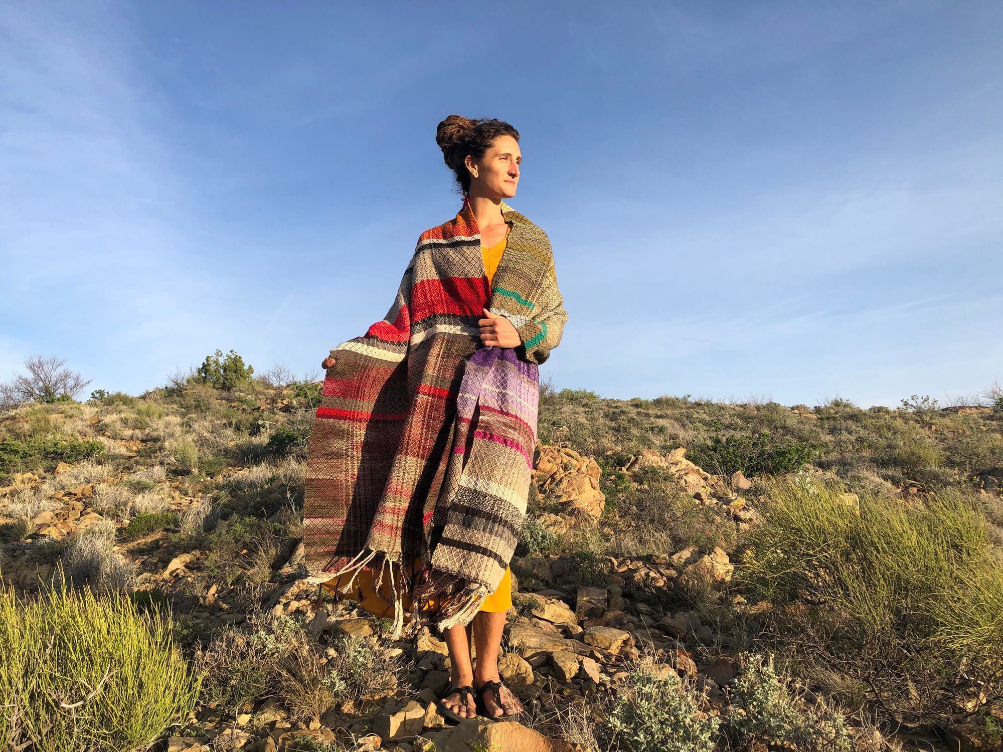 woman wearing Handwoven red, white, orange, green, purple, brown and black shawl standing in the desert