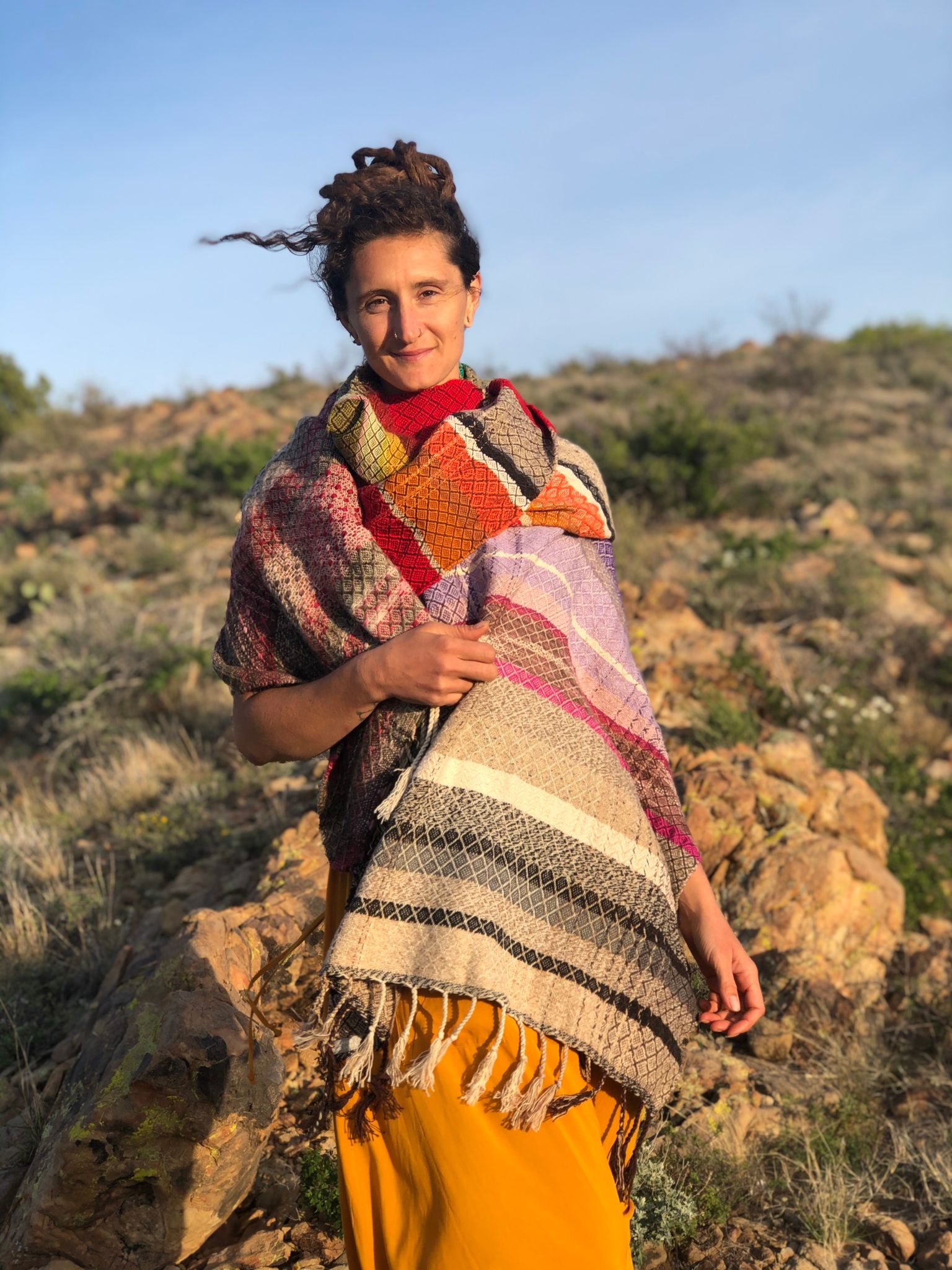 woman wearing Handwoven red, white, orange, green, purple, brown and black shawl standing in the desert