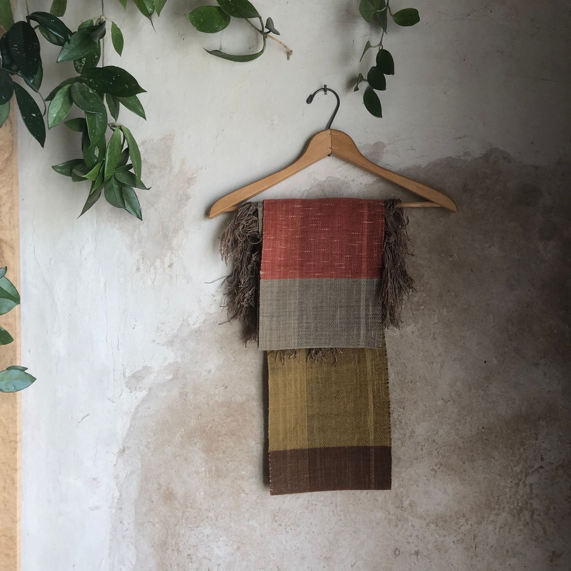 handwoven highly textured scarf that is mustard, brown, grey-blue and salmon colored, on a hanger against a wall