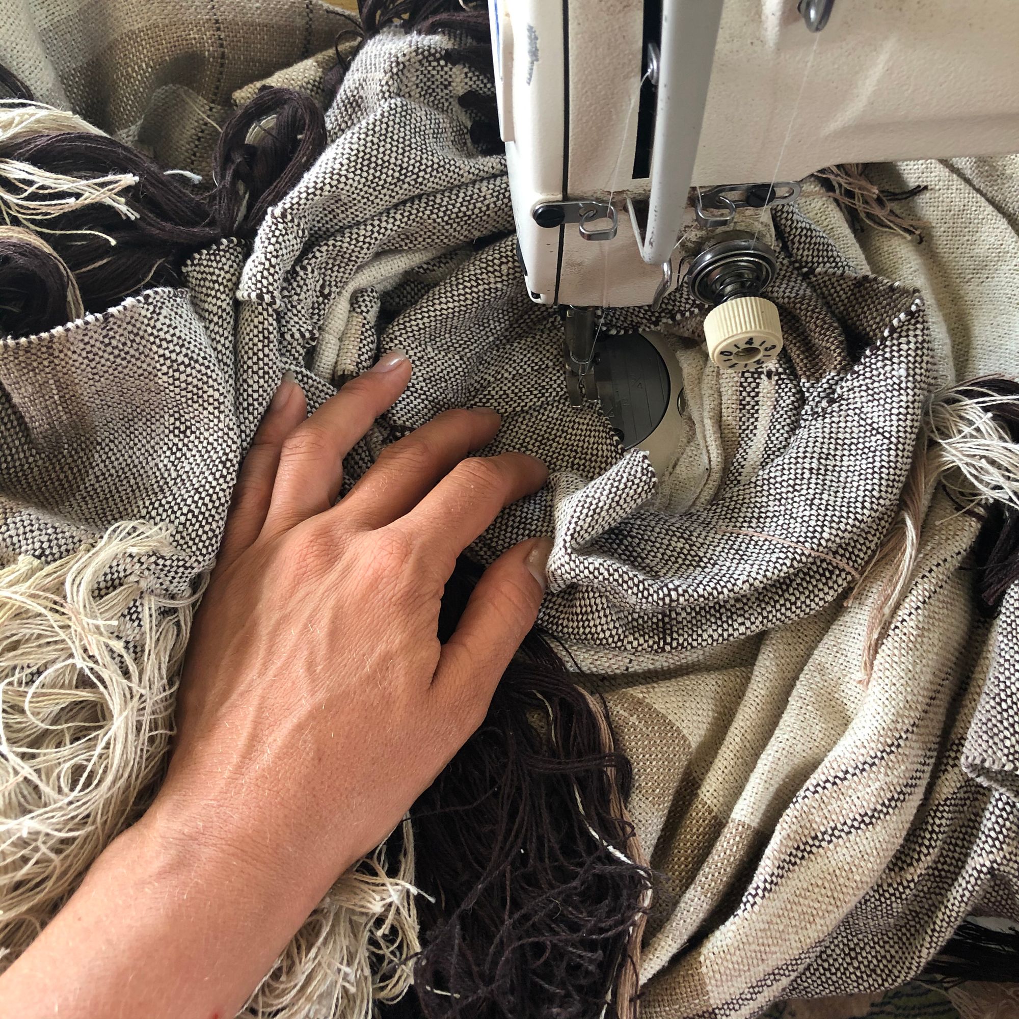 raw silk and organic cotton linen brown, tan and white Handwoven fringed Cloak being sewn on a sewing machine 