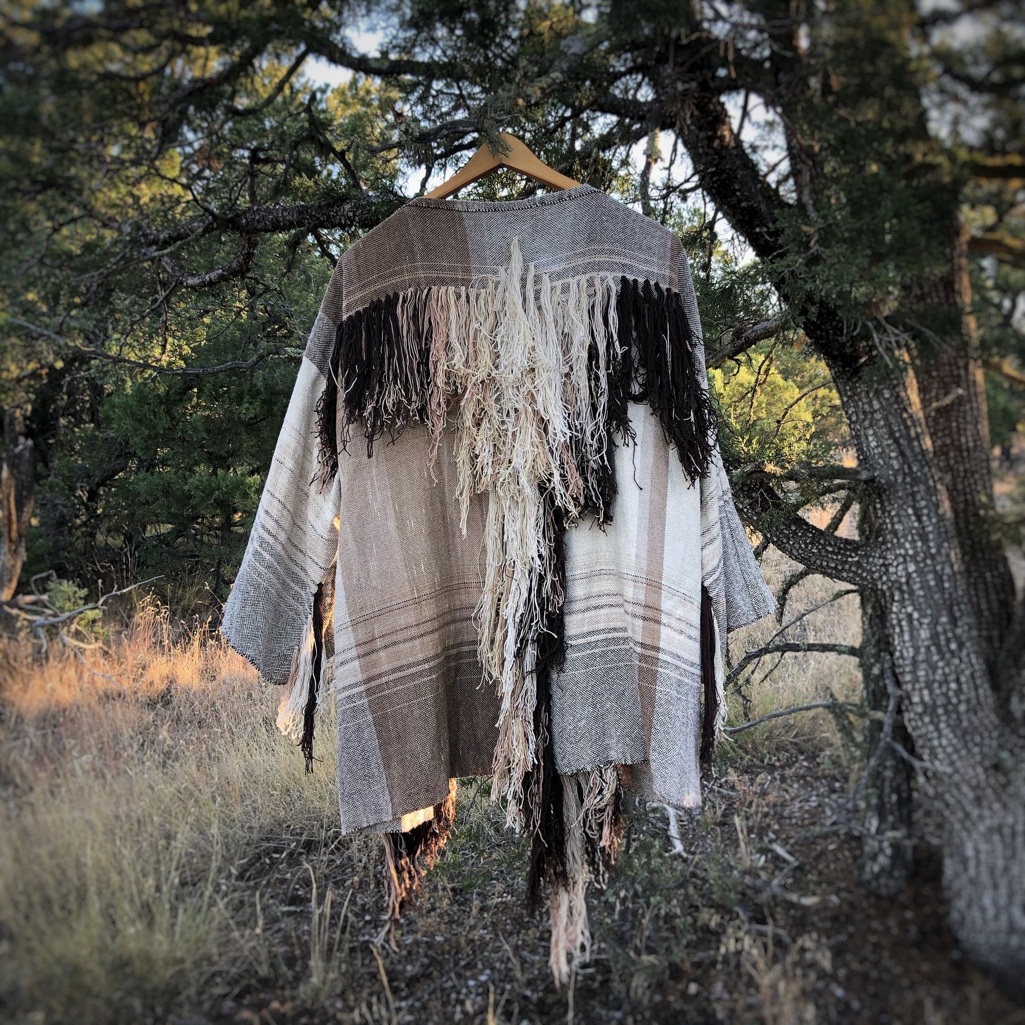 raw silk and organic cotton linen brown, tan and white Handwoven fringed Cloak hanging on a hanger in a tree