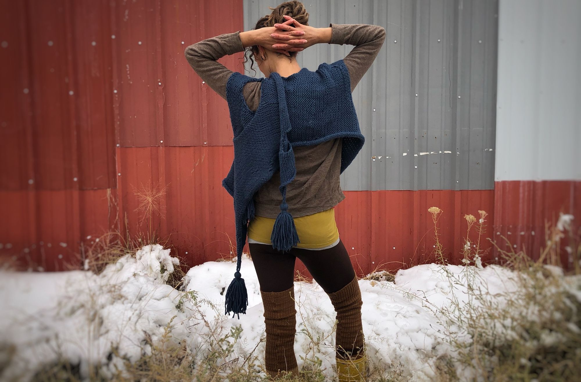 woman standing in snow wearing a blue knit shawl in front of a red and grey metal wall