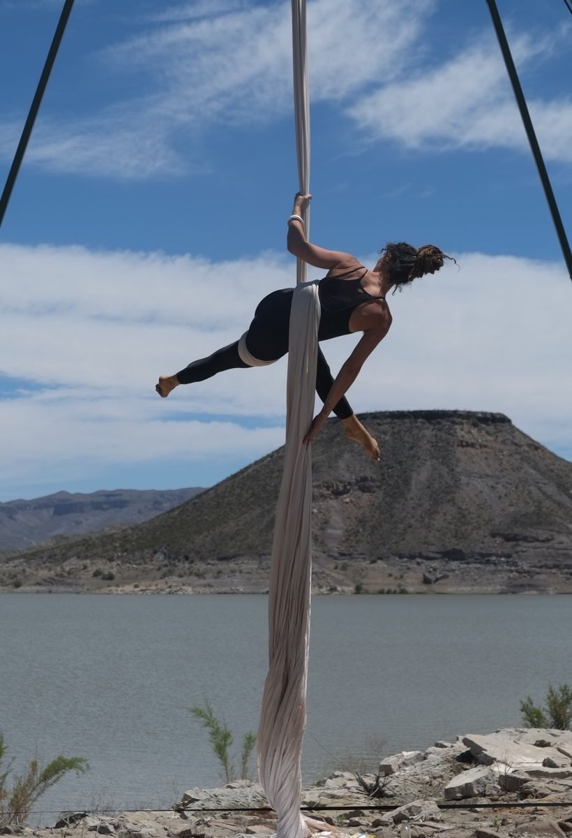 Woman doing aerial silks in front of a dramatic desert landscape. 